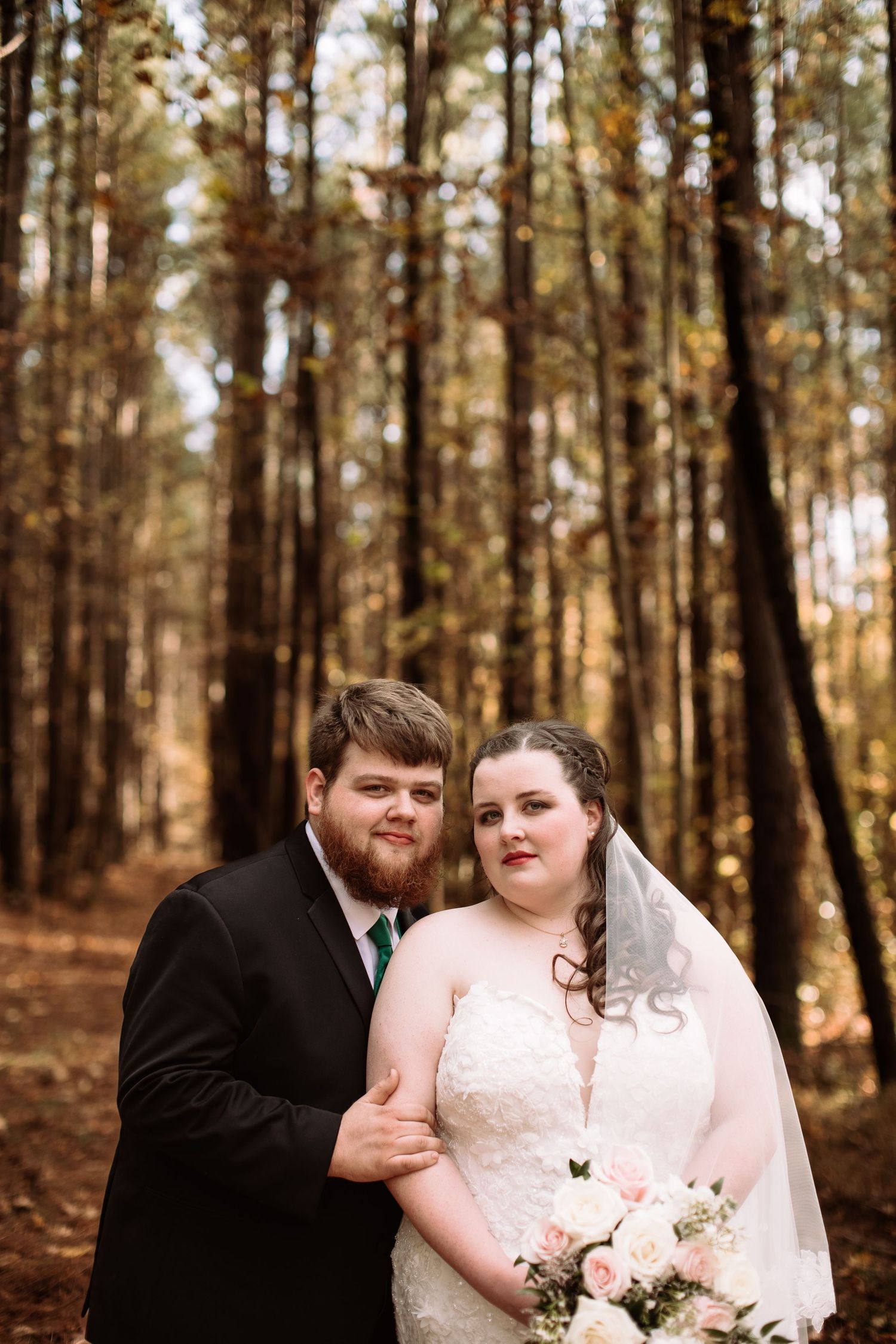 A romantic wedding photoshoot in a sunlit forest with pine trees creating a warm autumn atmosphere.