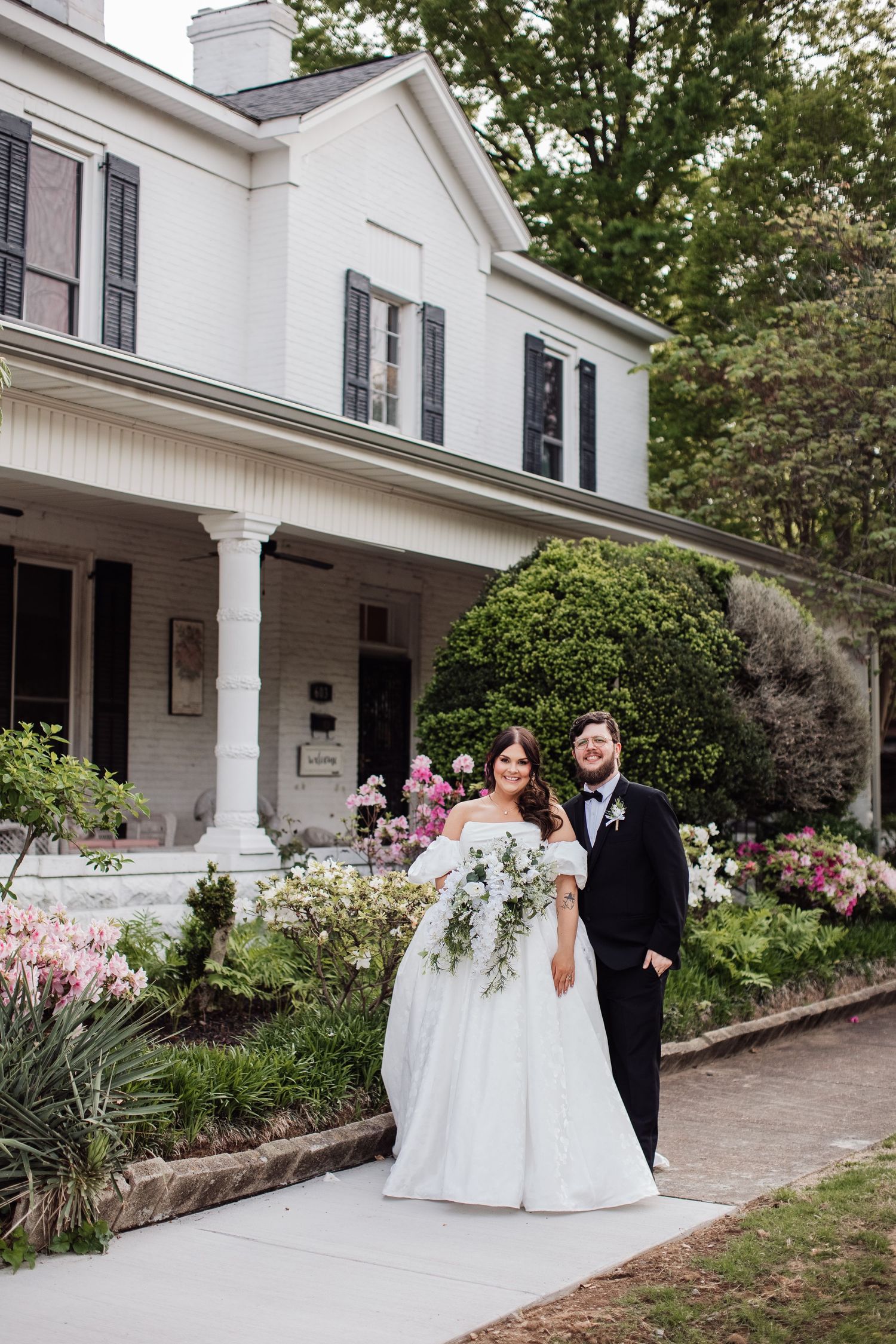 Elegant white wedding venue with a wrap-around porch and landscaped garden setting.