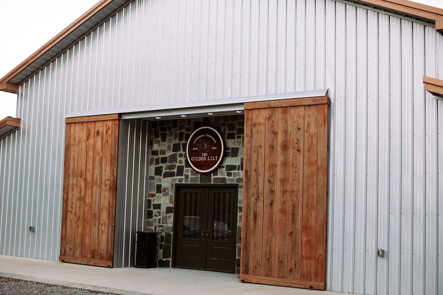 A rustic wooden barn door slides open to reveal a metal building interior with corrugated walls.