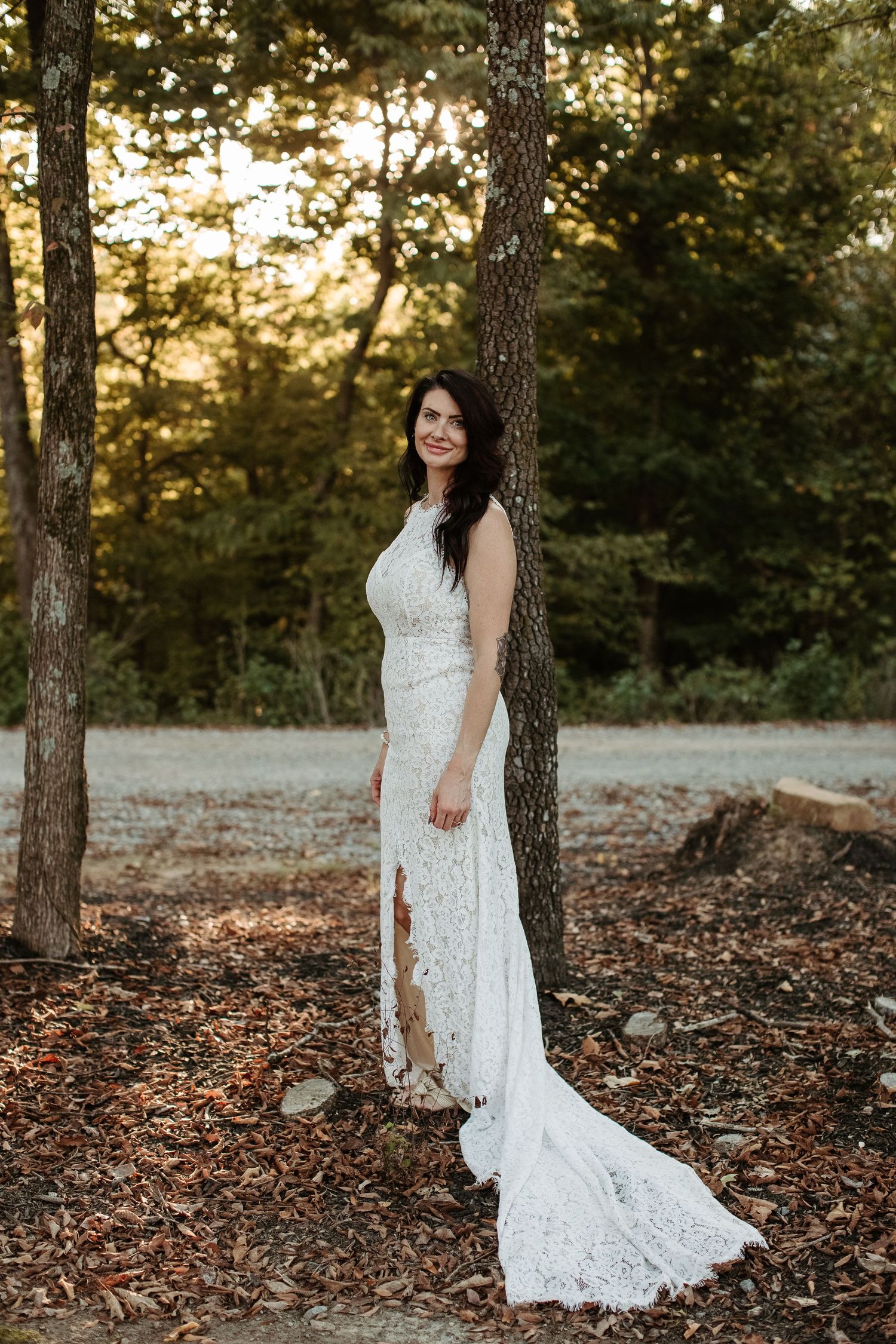 Beautiful lace wedding dress with long train photographed in a forest setting at golden hour sunset.