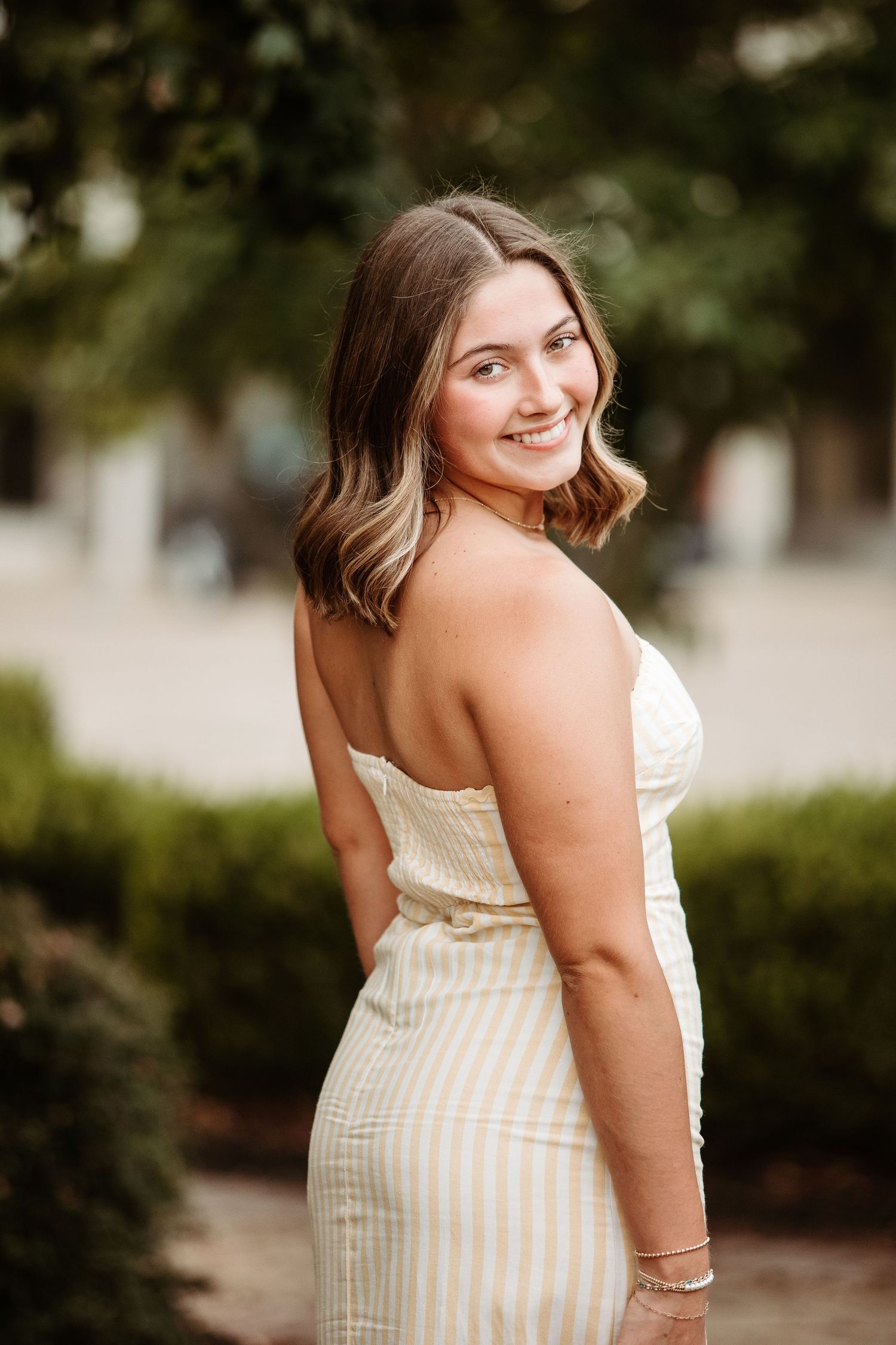 A person in a white striped sundress poses outdoors in a series of candid shots with natural lighting.