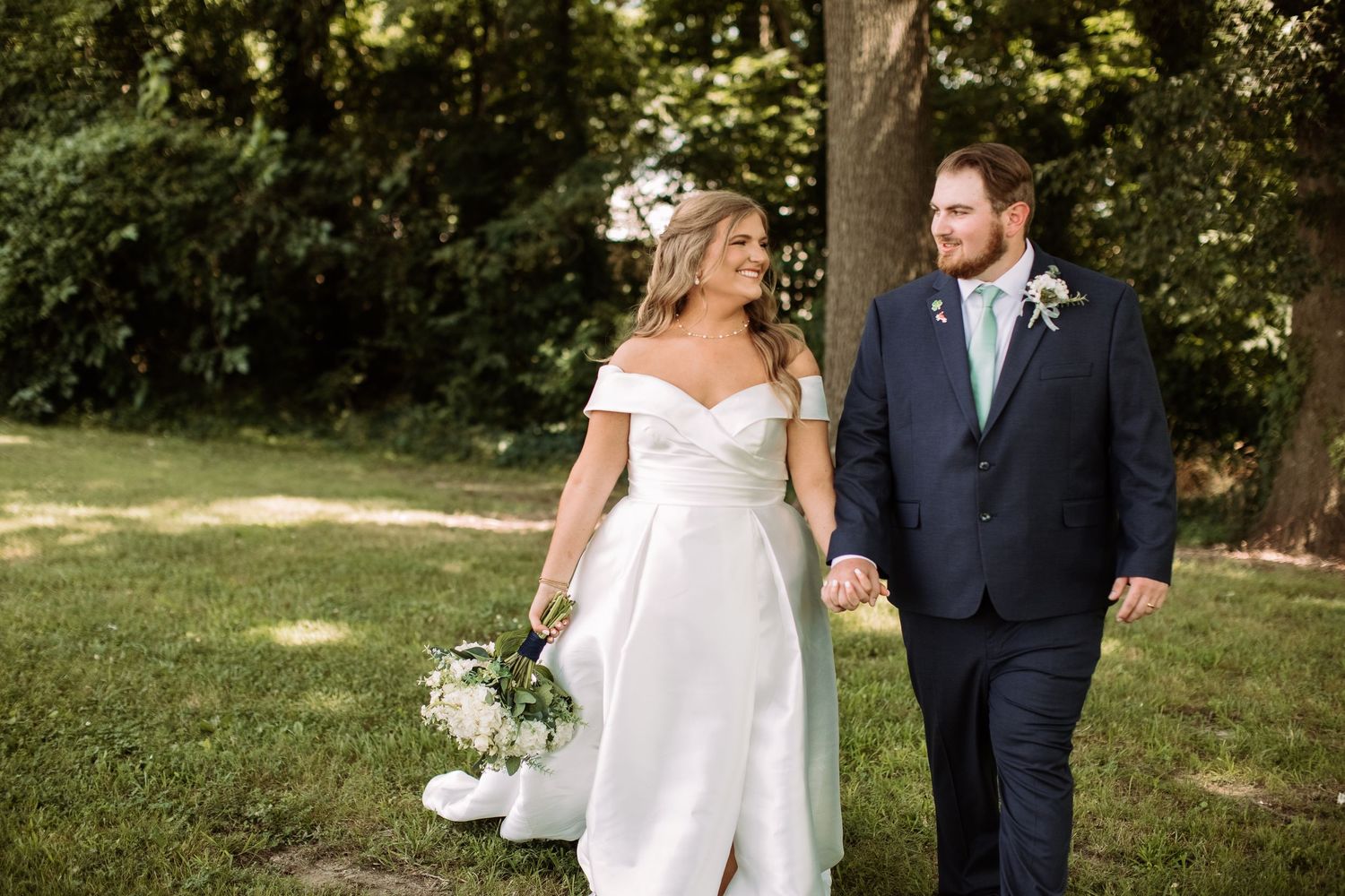 A couple in wedding attire walks together through a lush green garden setting on their special day.