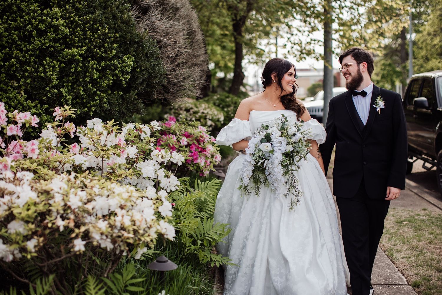 Elegant wedding couple poses in lush garden setting with beautiful floral arrangements and natural greenery.
