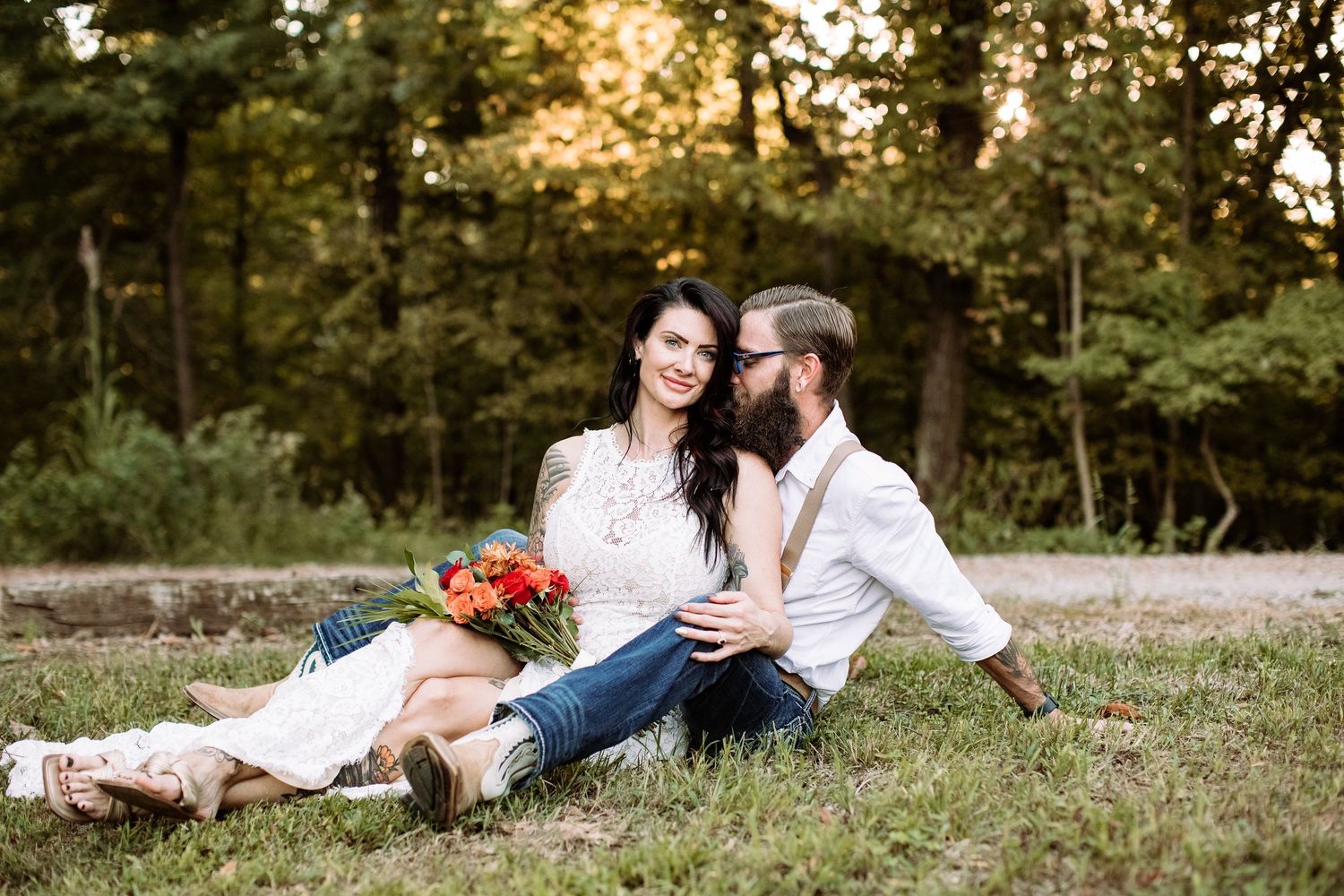 A couple shares an intimate moment while sitting together in a grassy field at sunset.