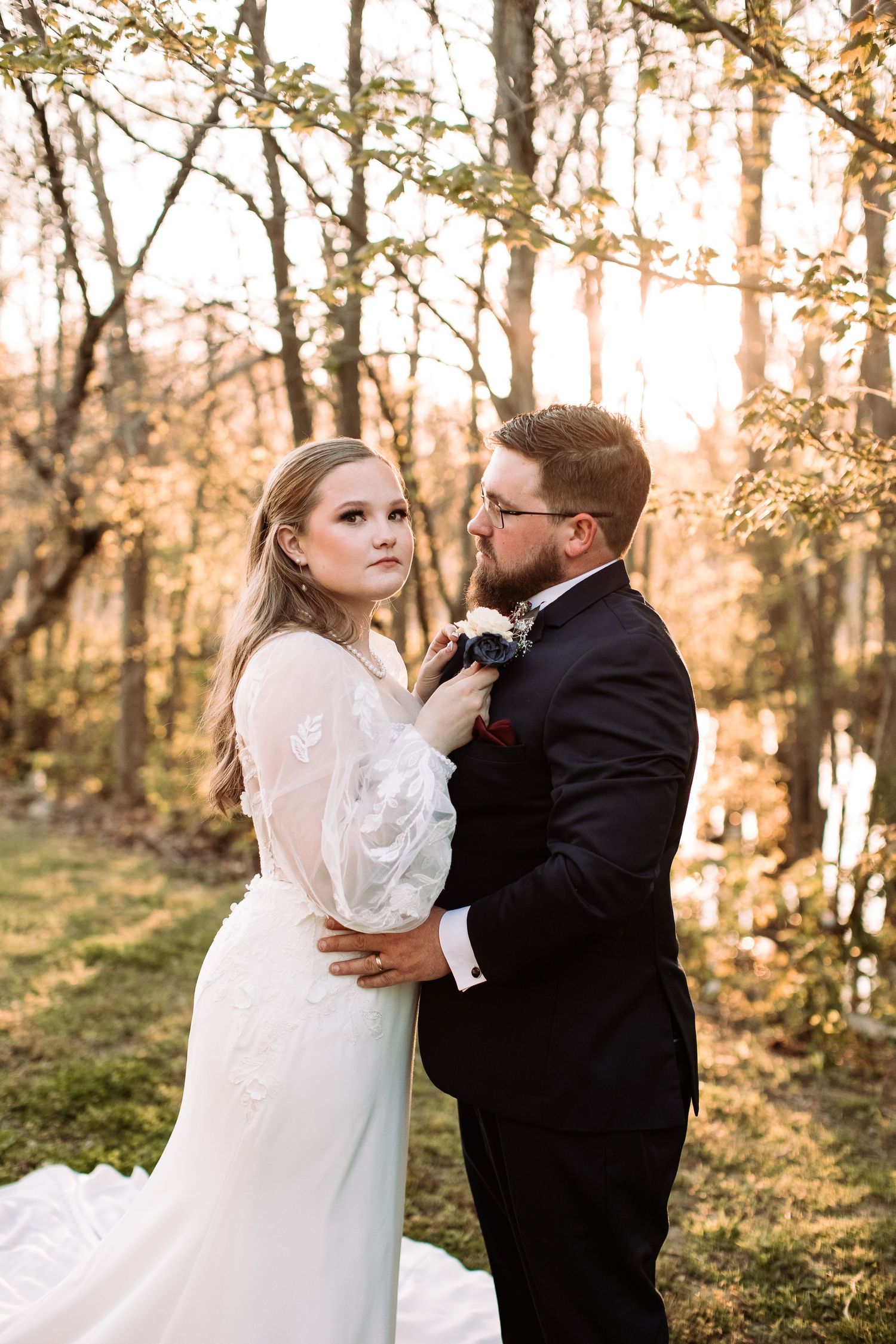 A romantic wedding couple embraces in a sunlit forest setting during golden hour.