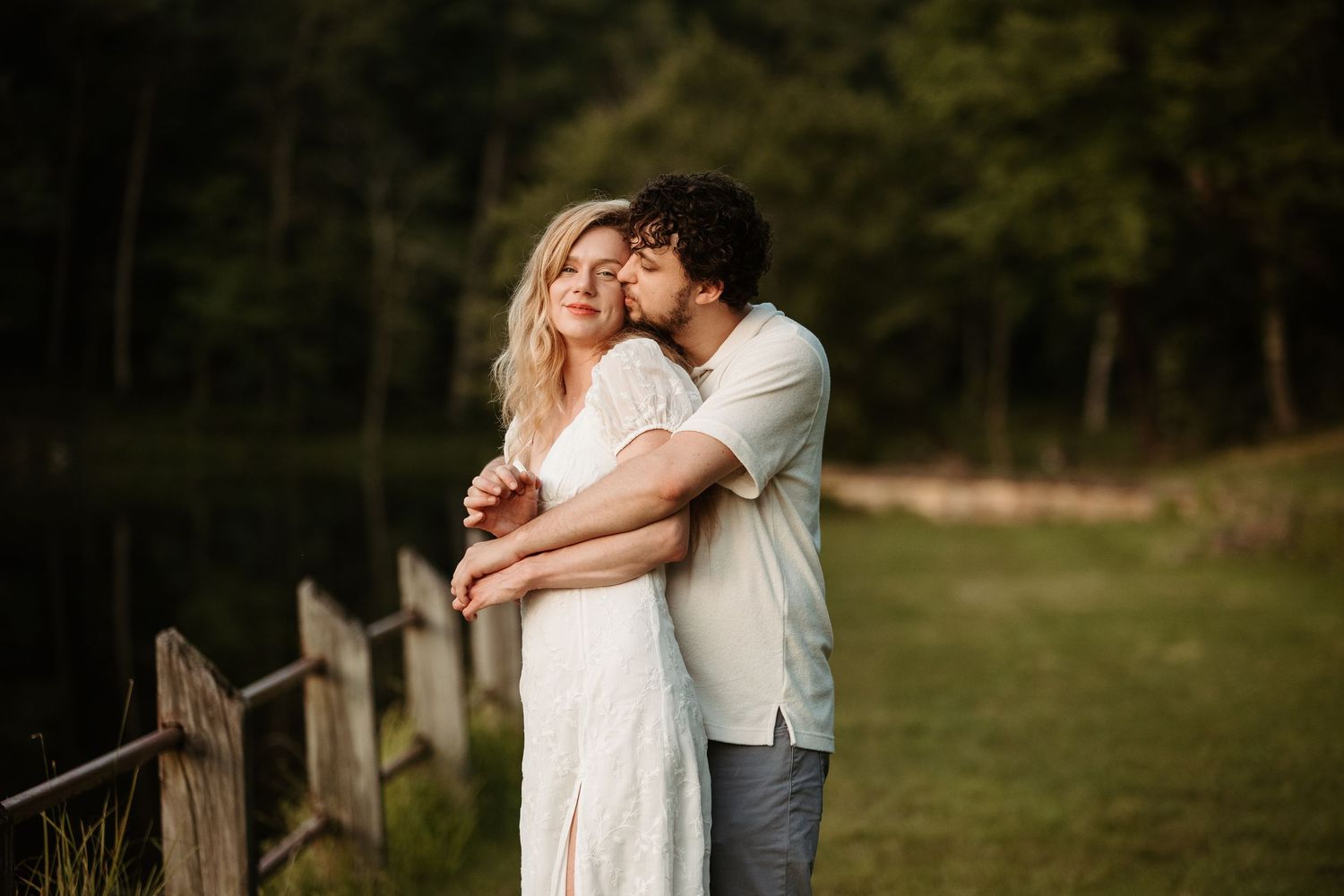 A romantic couple embraces in a golden sunset field wearing white and gray casual attire.
