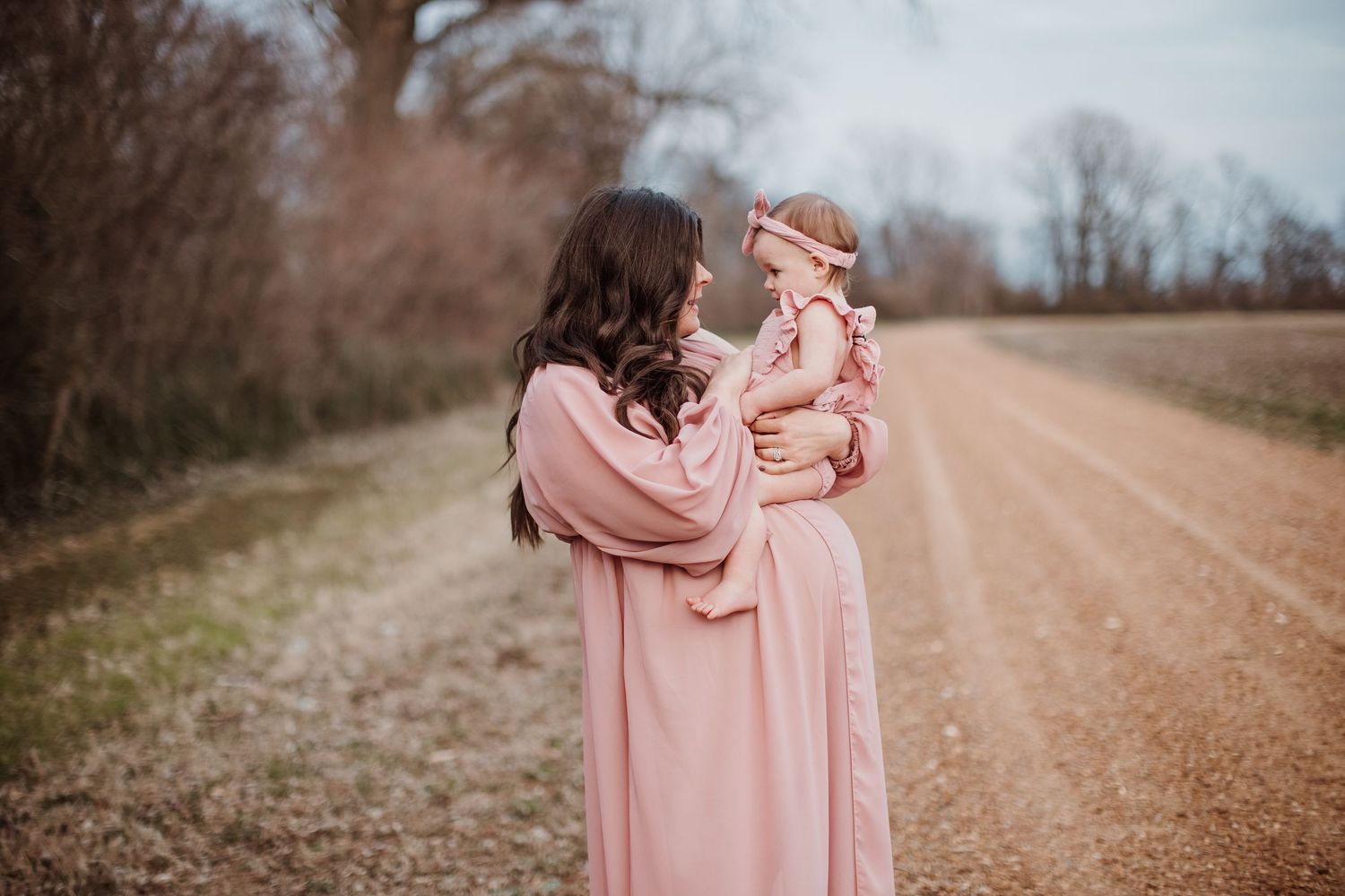 A tender moment between mother and child wearing matching pink dresses on a rural dirt road.
