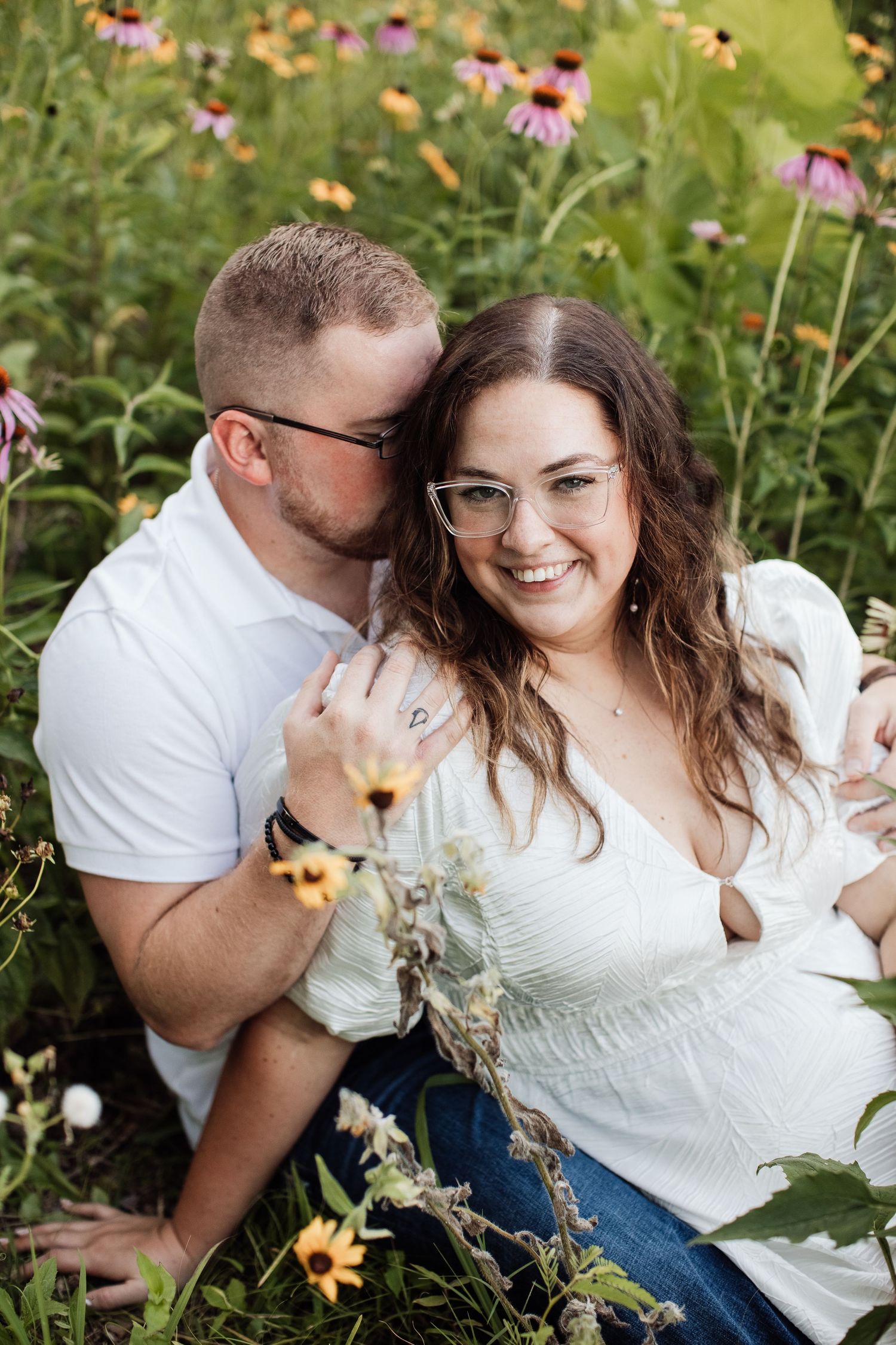 A happy couple shares a tender moment while sitting among blooming coneflowers in a summer garden.