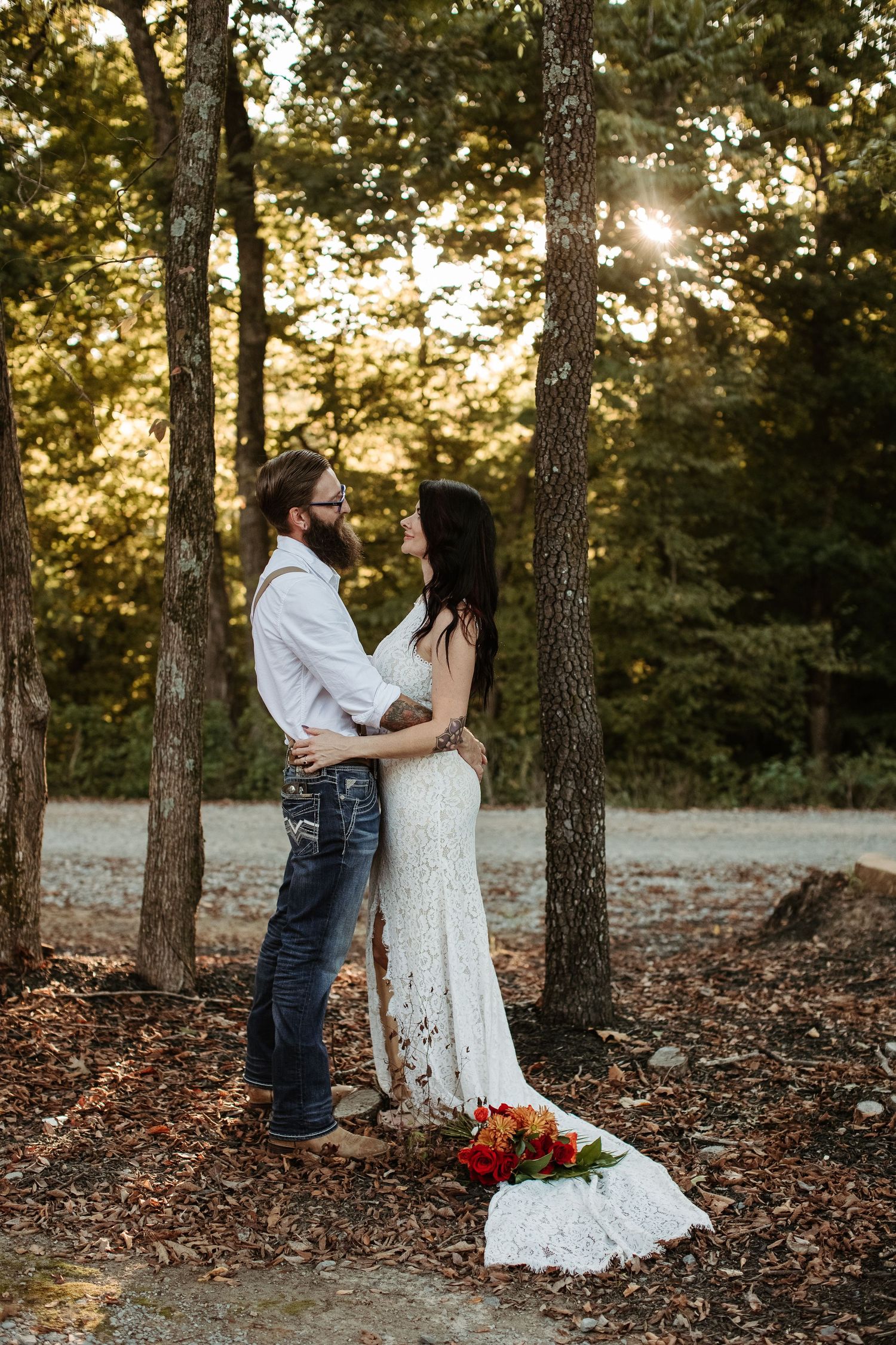 A romantic couple shares a tender moment among tall pine trees at sunset in a wooded forest setting.
