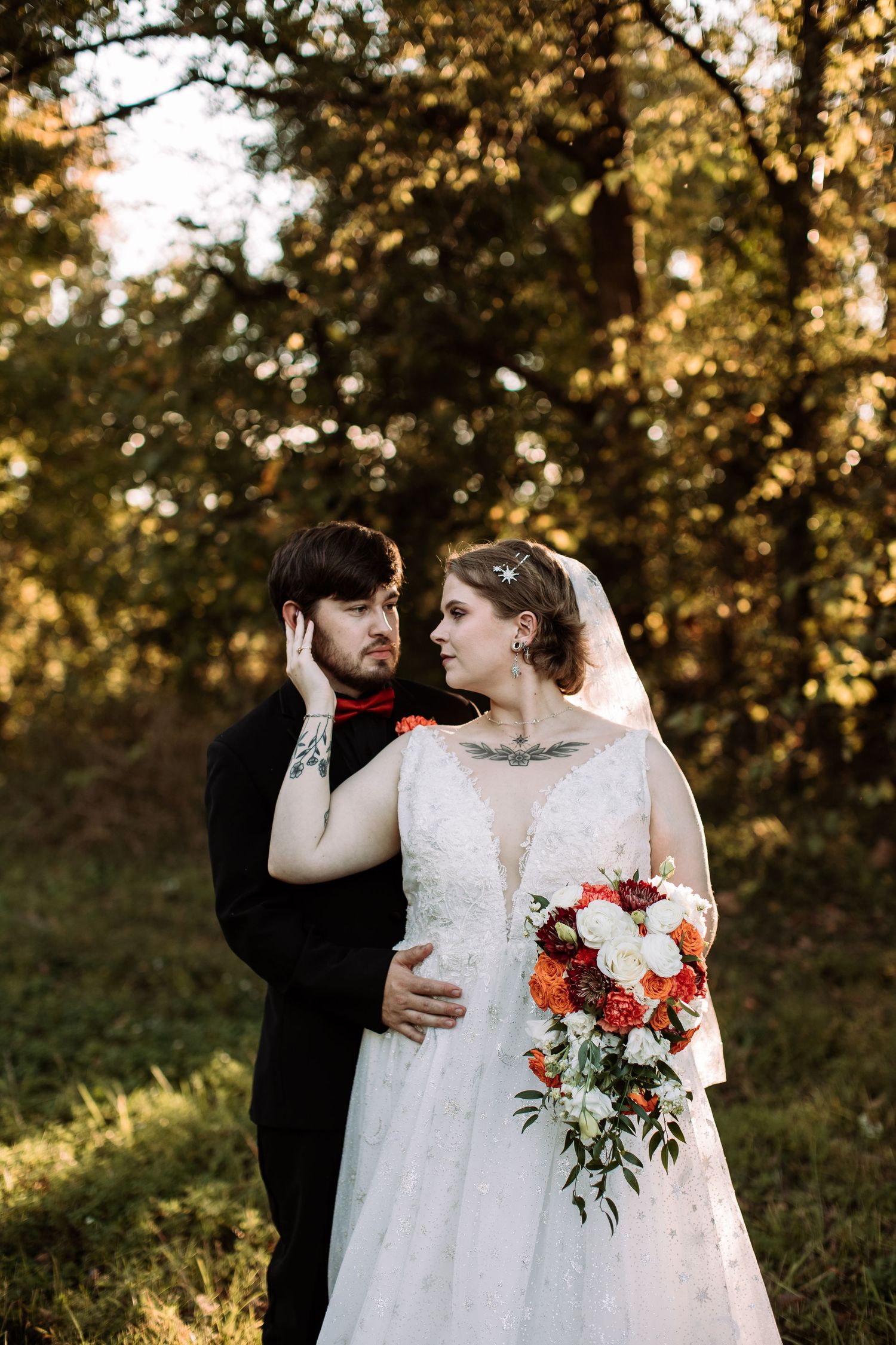 A couple embraces during their outdoor autumn wedding ceremony with golden sunlight filtering through trees behind them.