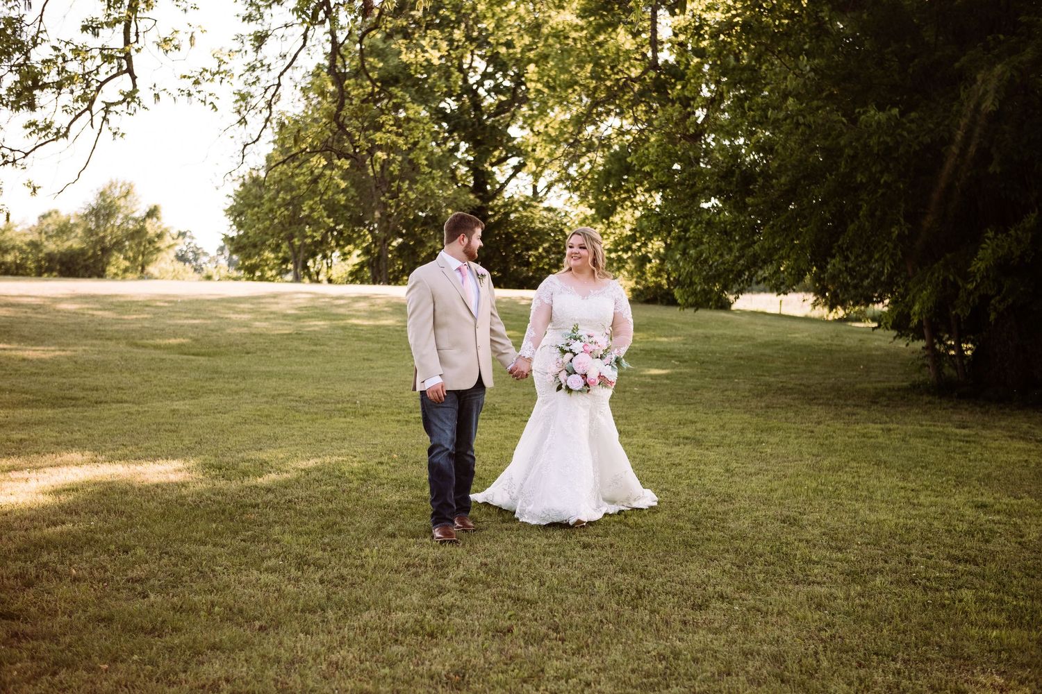 Bride and groom holding hands walking on lush green lawn outdoors on their wedding day.