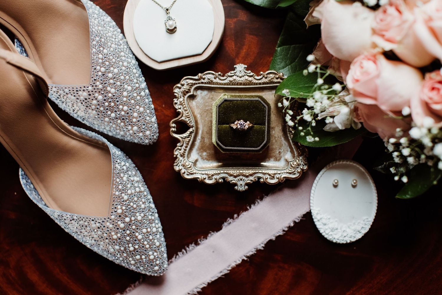 Wedding rings and engagement ring displayed with floral decor and sparkly accessories on dark wooden surface.
