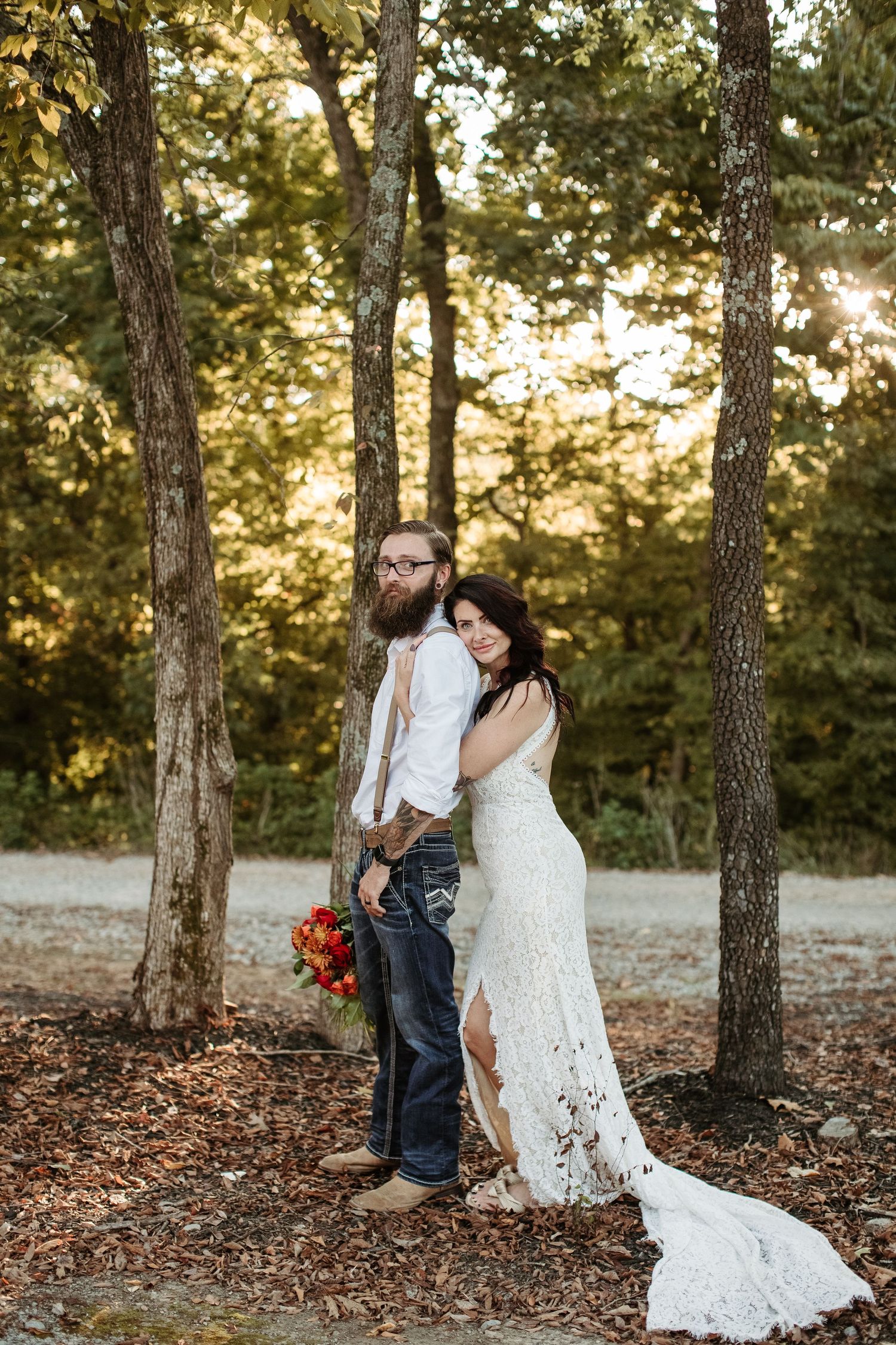 A couple shares a romantic moment in a sunlit forest setting with fall foliage and tall pine trees.