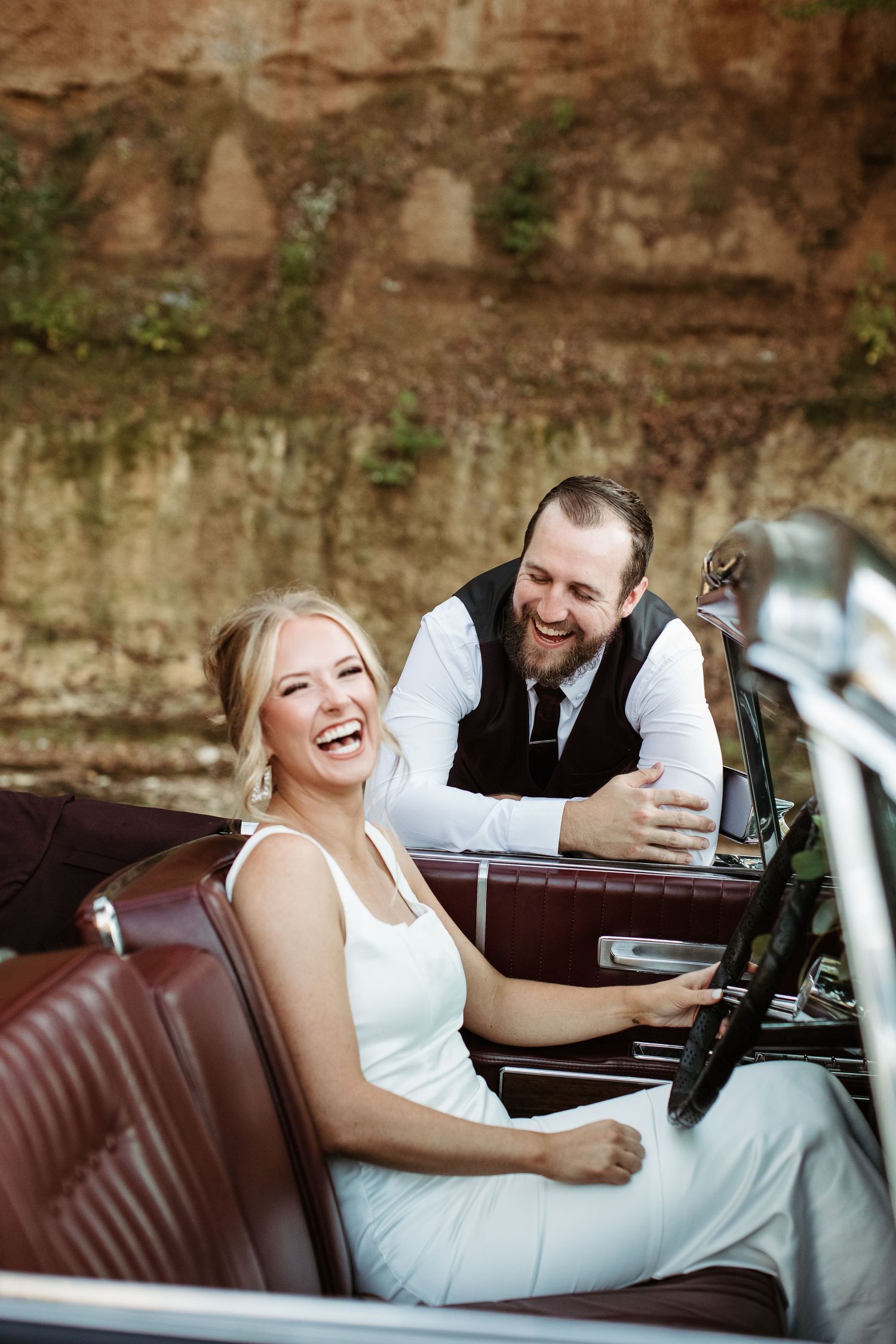 Couple lounging together in a classic vintage car with brown leather seats during a photo session.