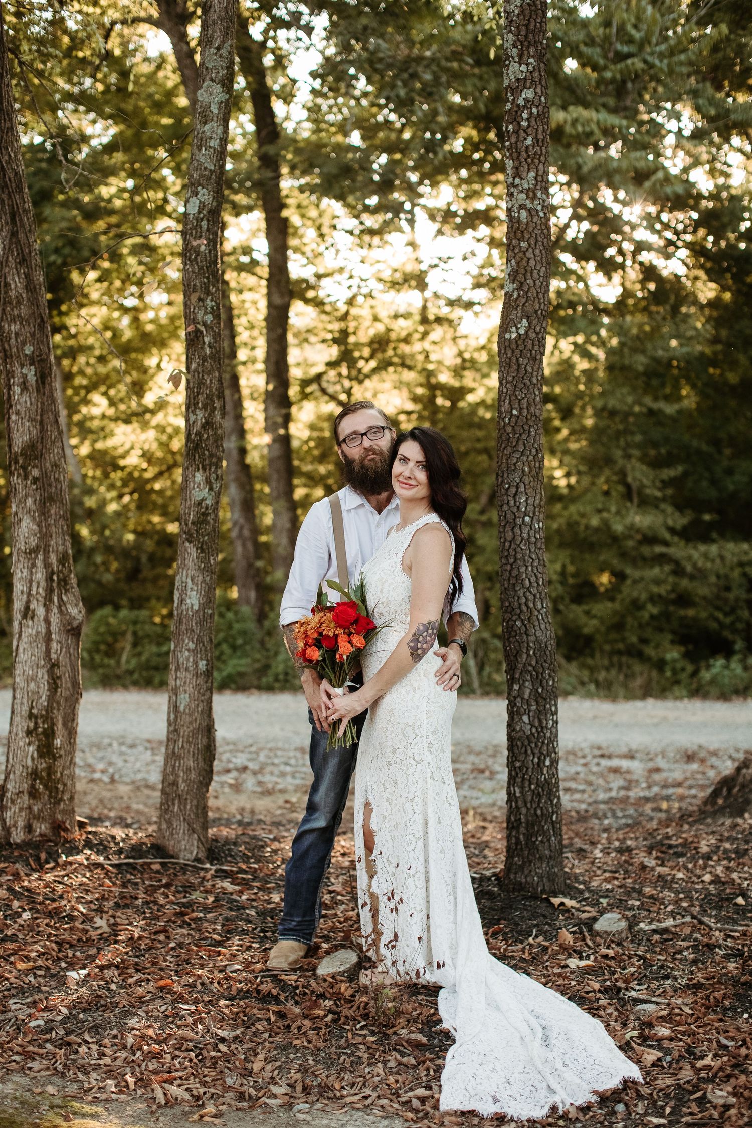 A romantic wedding couple embraces among tall pine trees during a golden sunset in a forest setting.