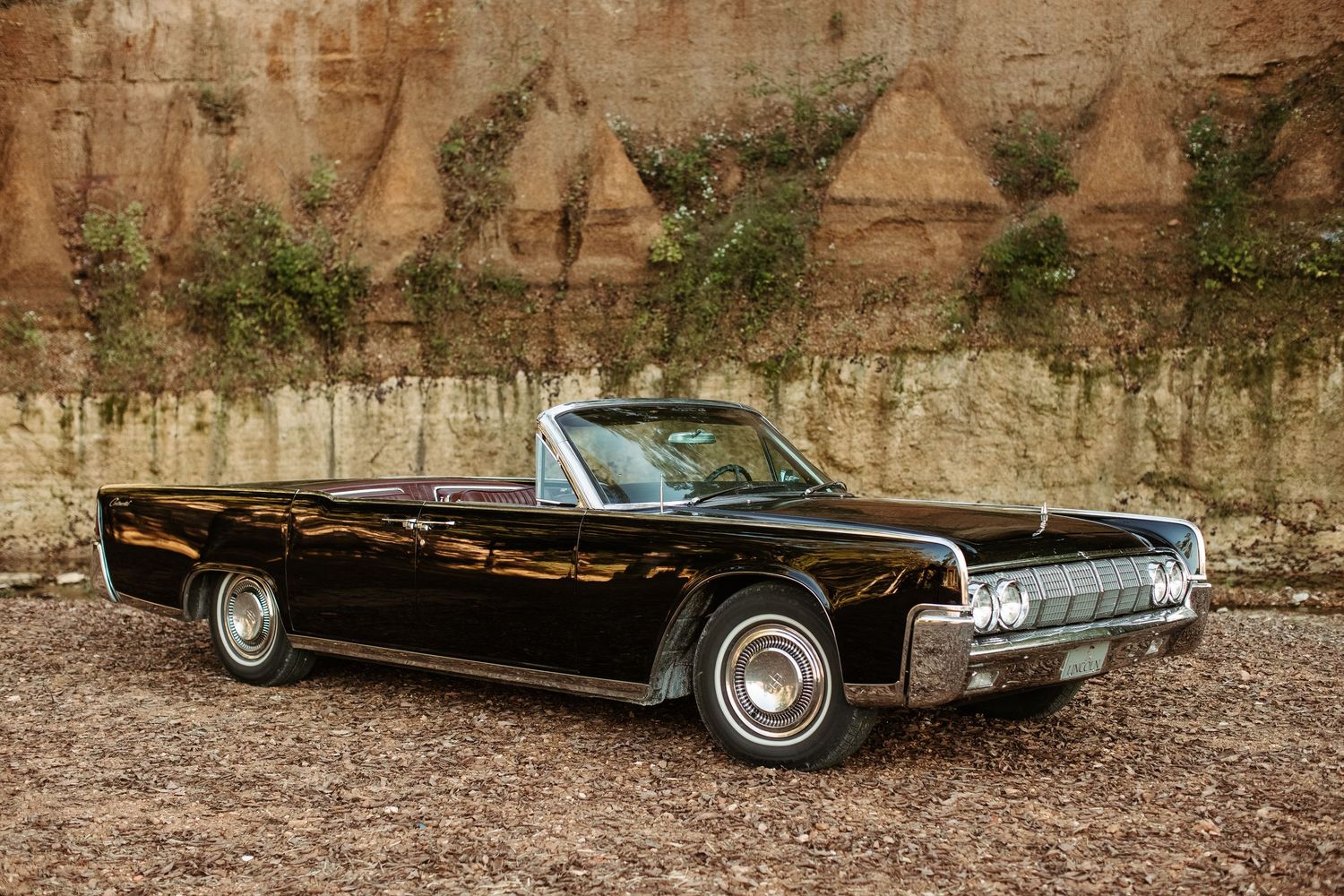 Classic black Lincoln Continental convertible with white wall tires parked against a textured stone wall.