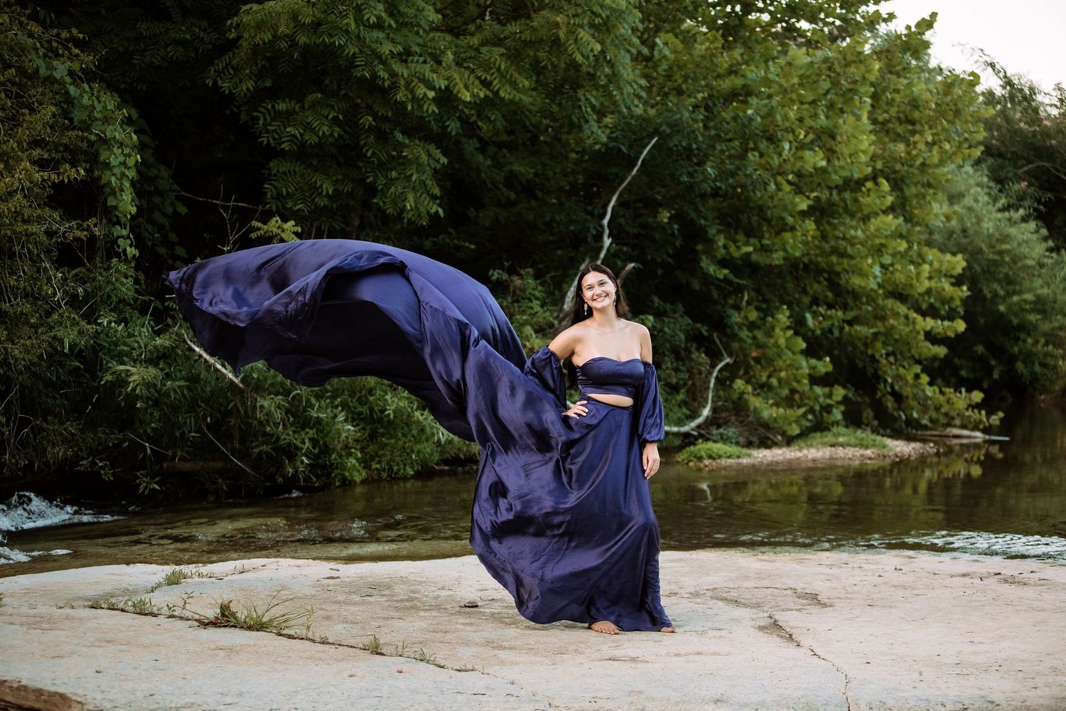 A person in a navy blue dress performs a series of graceful dance movements outdoors on a sandy beach area.