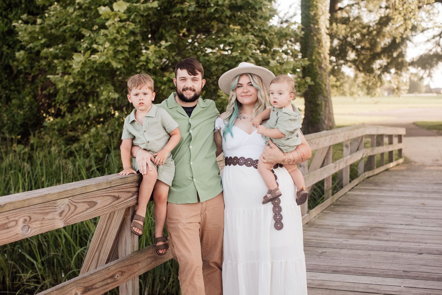 A loving family poses together on a wooden boardwalk surrounded by nature on a sunny afternoon.