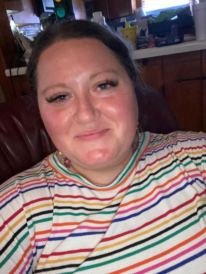 A person wearing a colorful striped sweater with rainbow horizontal stripes takes a selfie while smiling warmly at the camera.