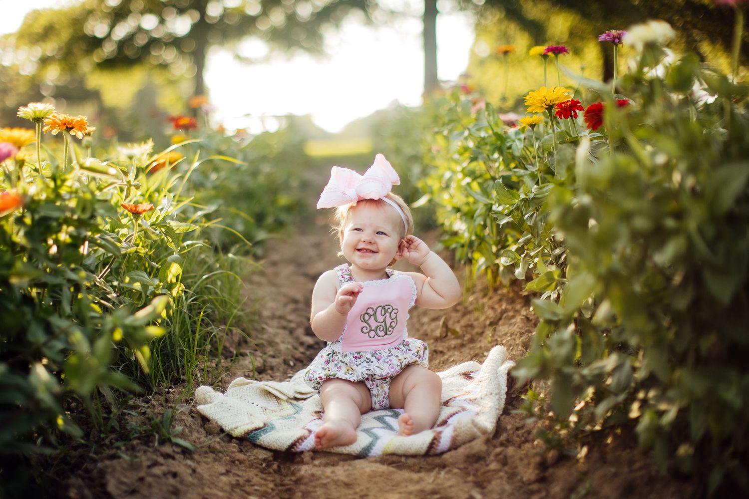 A child sits on a blanket in a garden path surrounded by blooming yellow and orange flowers.