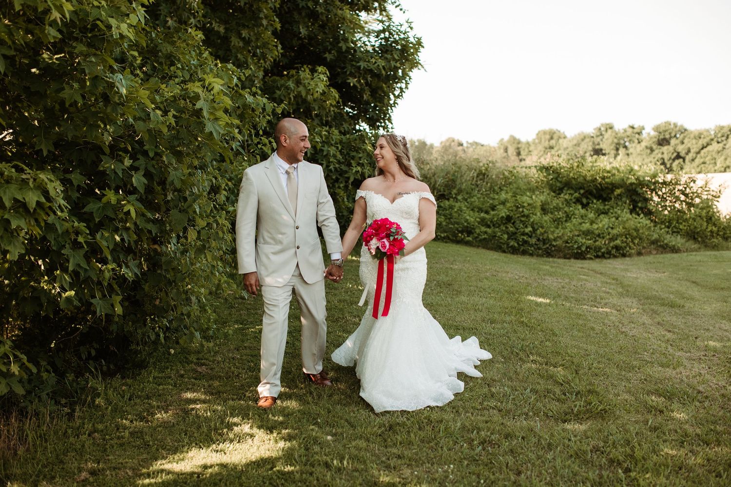 A couple in wedding attire poses together in a scenic outdoor garden setting during a summer celebration.