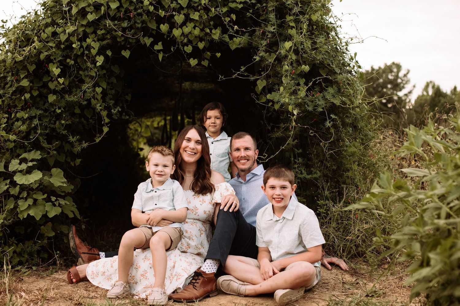 A family group poses together under a lush green archway of foliage on a summer day.