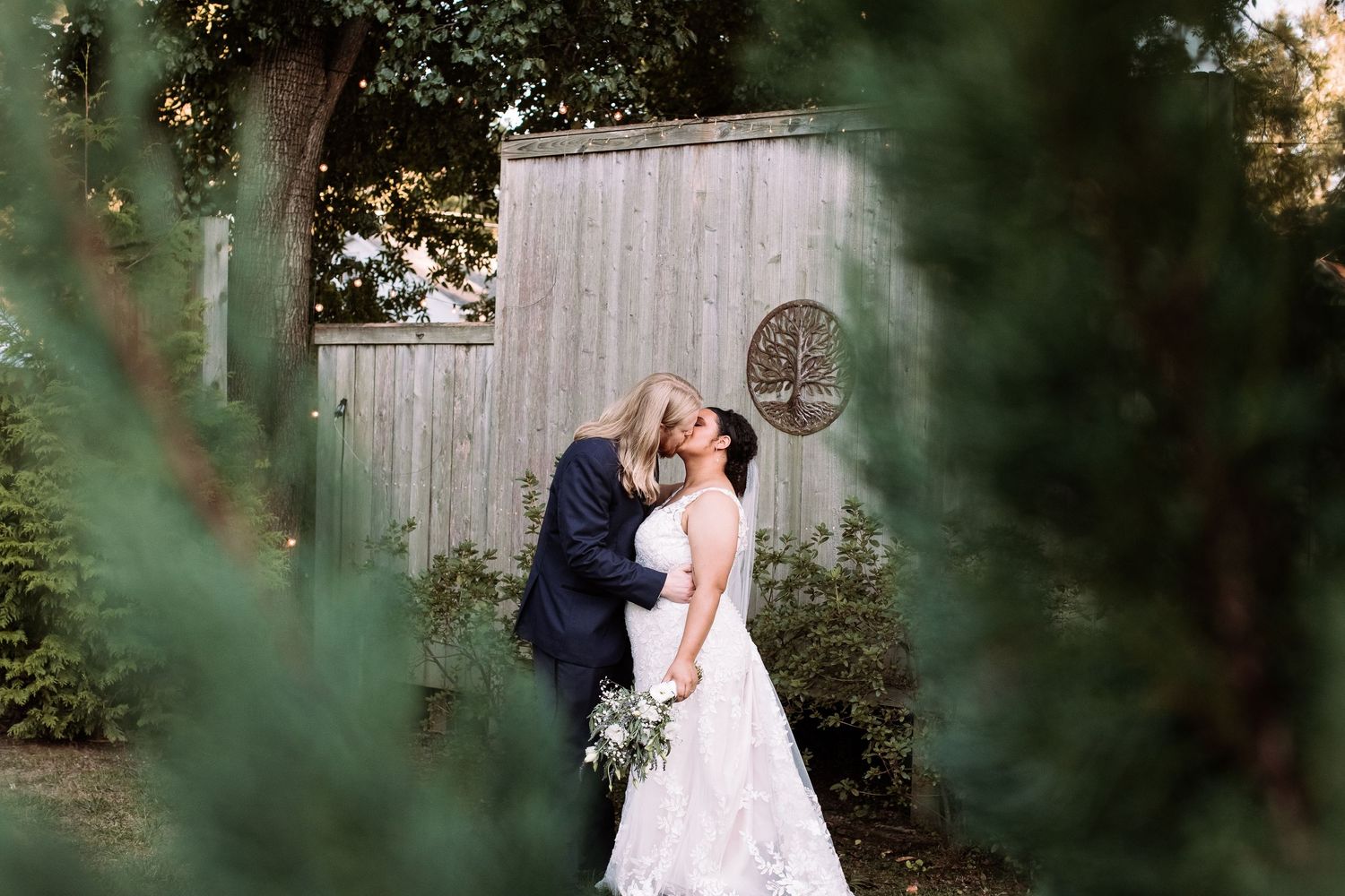 Romantic couple embraces in a garden setting with soft natural lighting and lush greenery in the background.