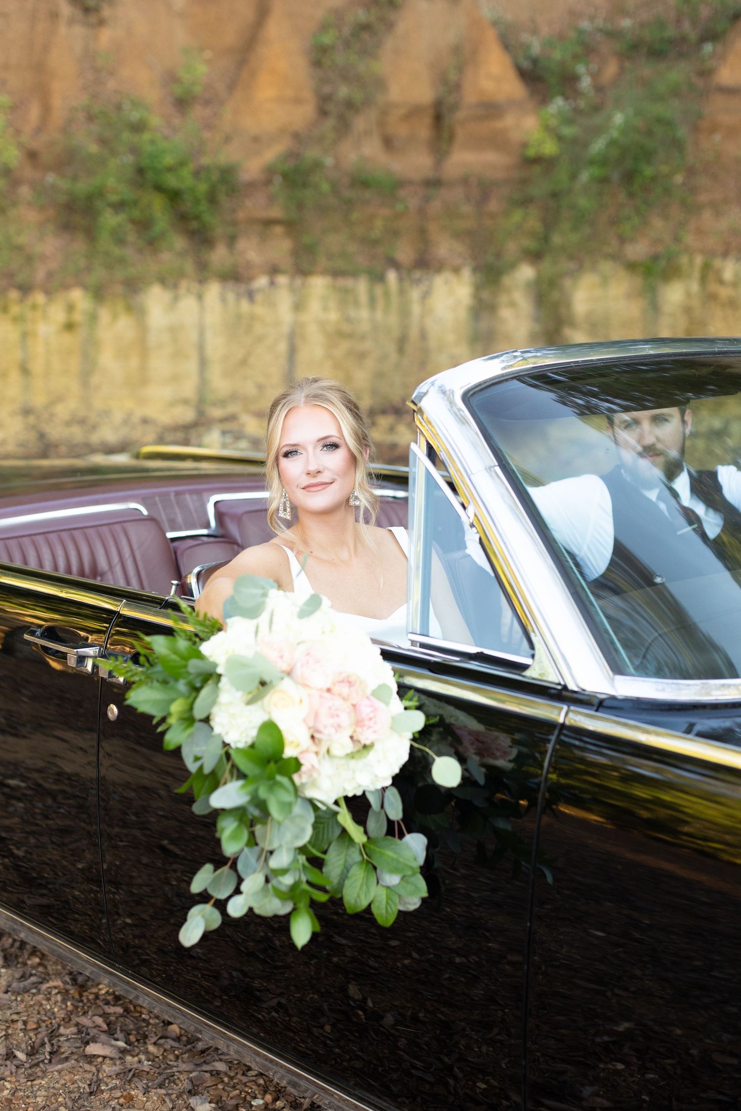 Vintage black car decorated with white flowers and eucalyptus leaves for a wedding celebration.