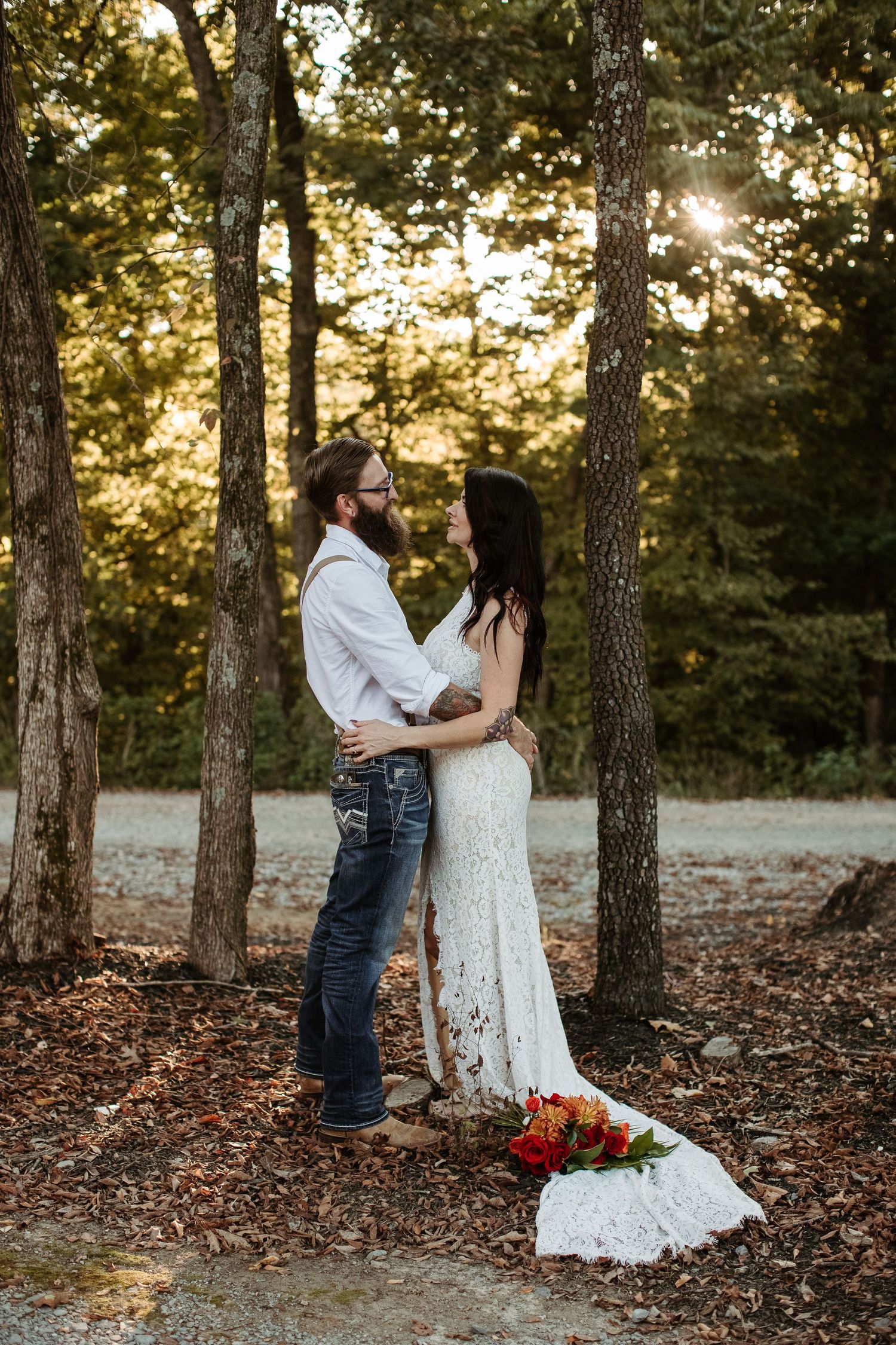 A couple in a rustic forest setting share romantic moments during a fall wedding photoshoot at sunset.