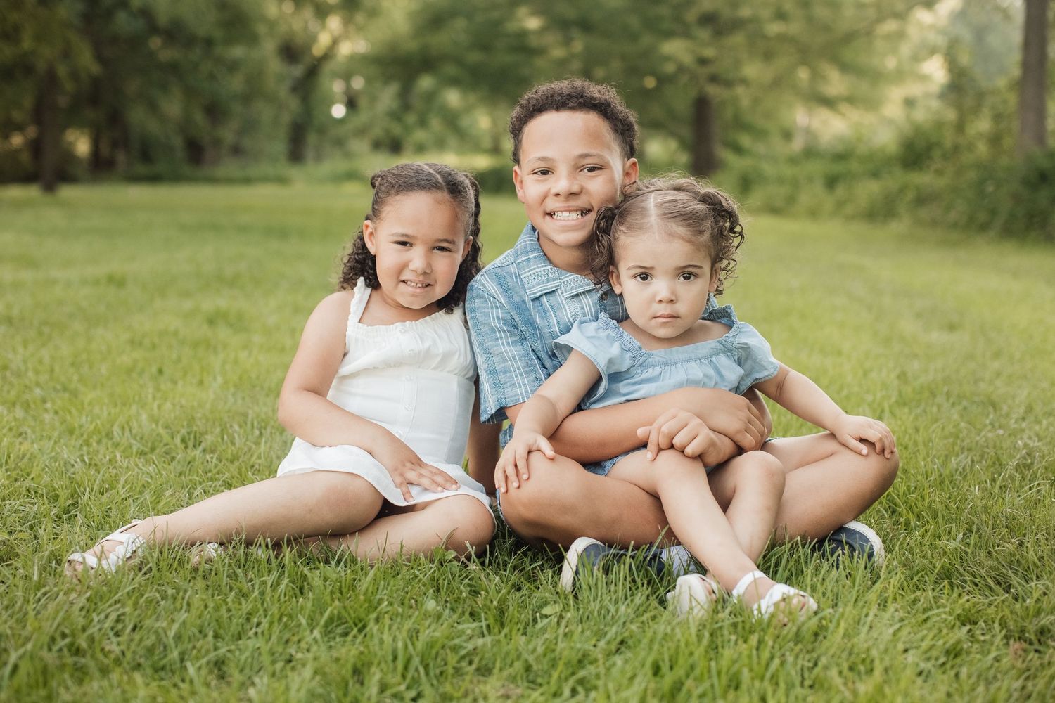 A family sits together in casual clothing on lush green grass during a warm sunny day outdoors.