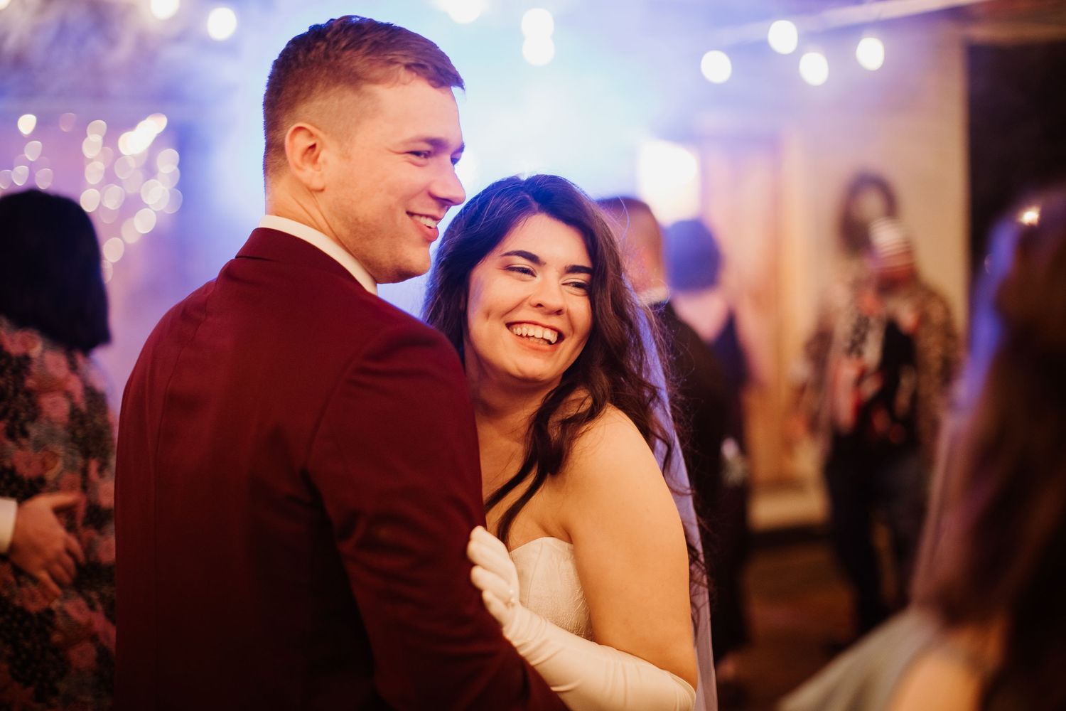 Bride and groom sharing a joyful first dance at their wedding reception with warm bokeh lights in background.