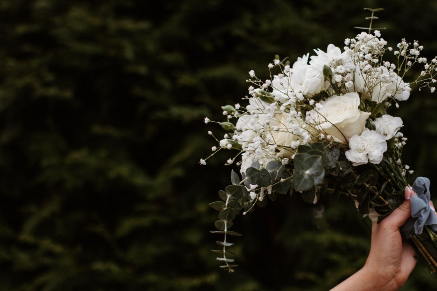A person holding a delicate white floral bouquet with cascading baby's breath and roses against a dark background.