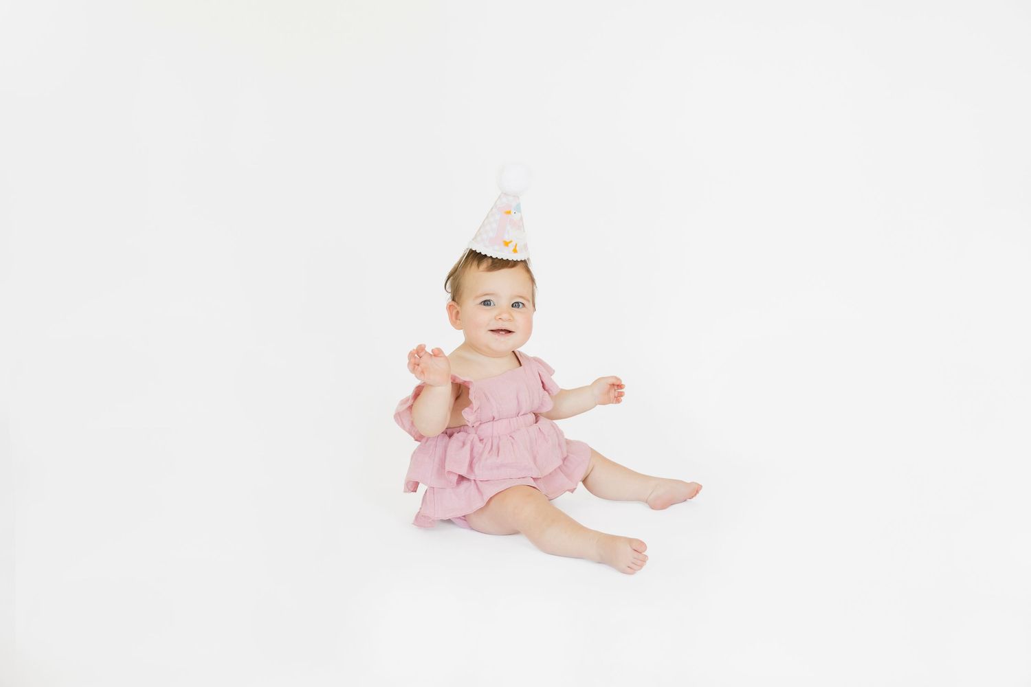 Baby in pink ruffled outfit crawling and smiling on white background.