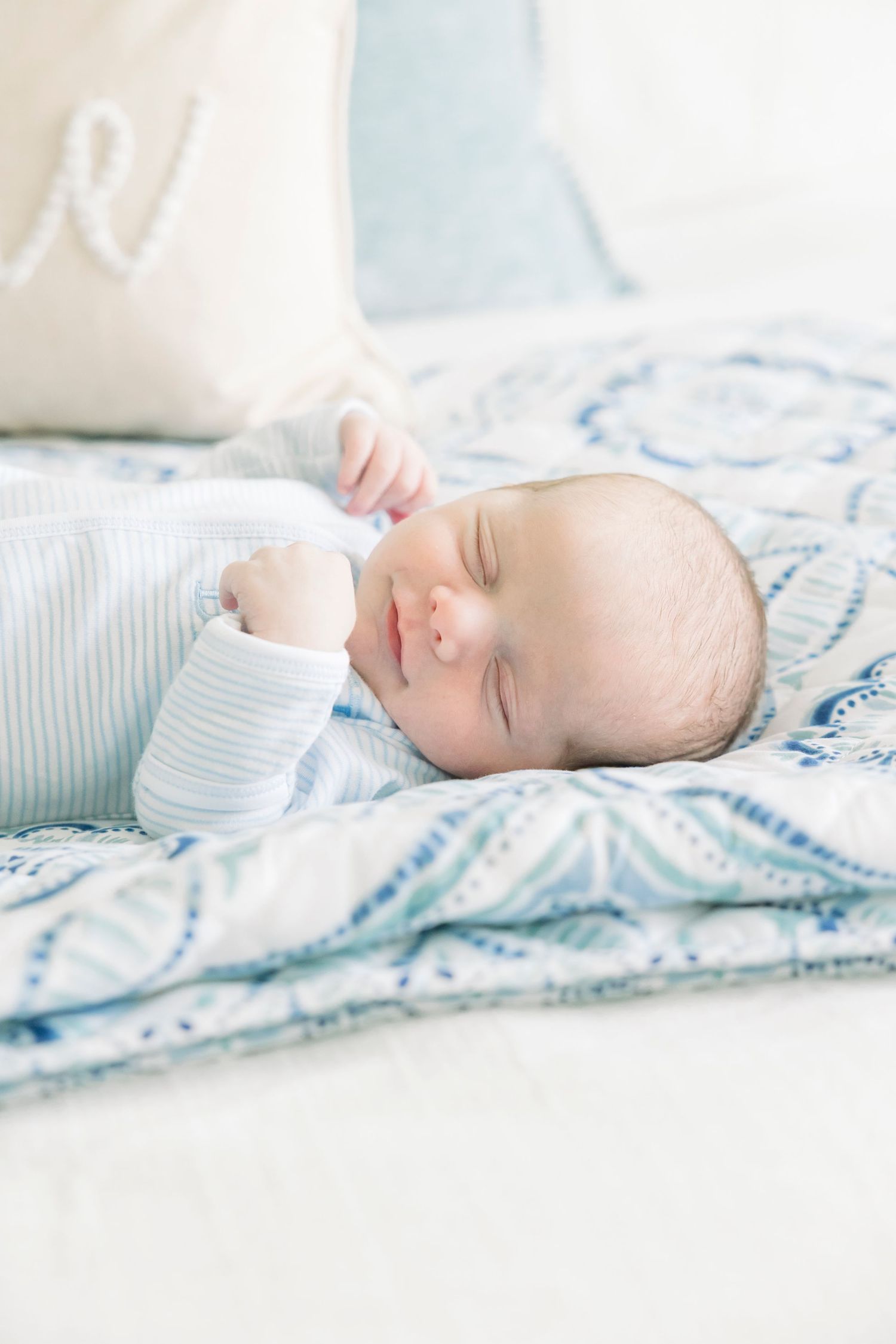 Sleeping baby in light blue outfit rests peacefully on patterned bedding.