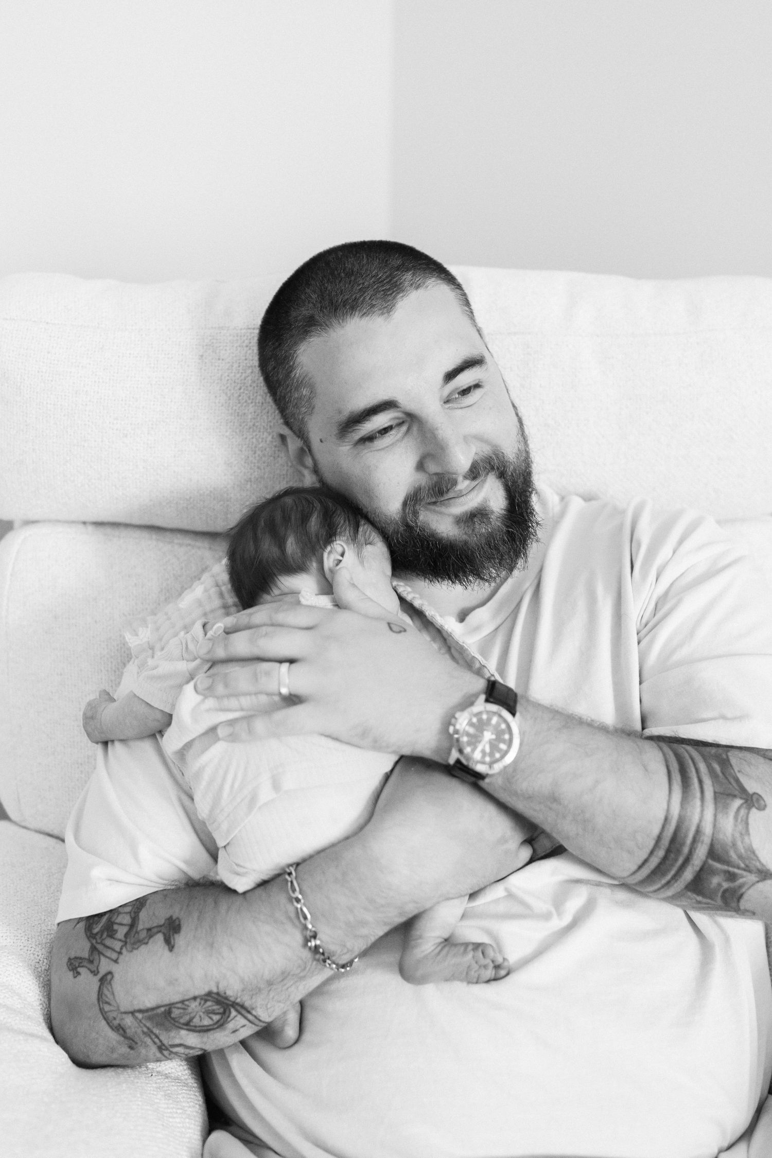 Black and white portrait of tender moment with infant resting on white bedding.