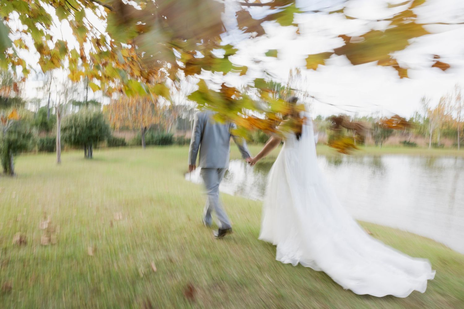 White wedding dress billows in the wind as couple dances in an autumn field.