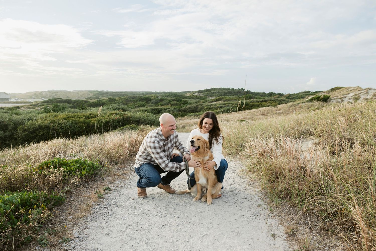 Couple walking their golden retriever along a scenic coastal trail at sunset.