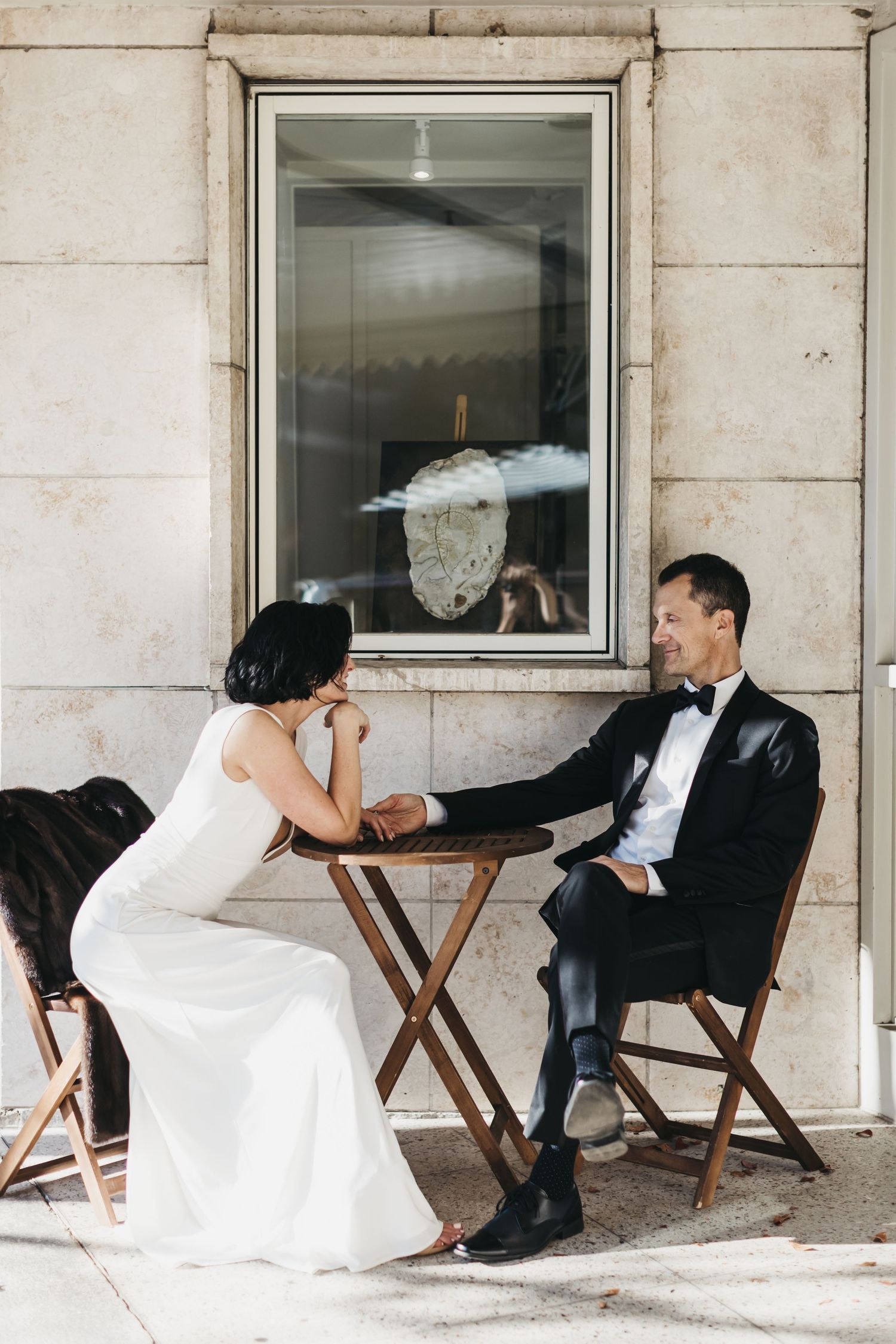 Playful wedding photo sequence on chairs against white building exterior.