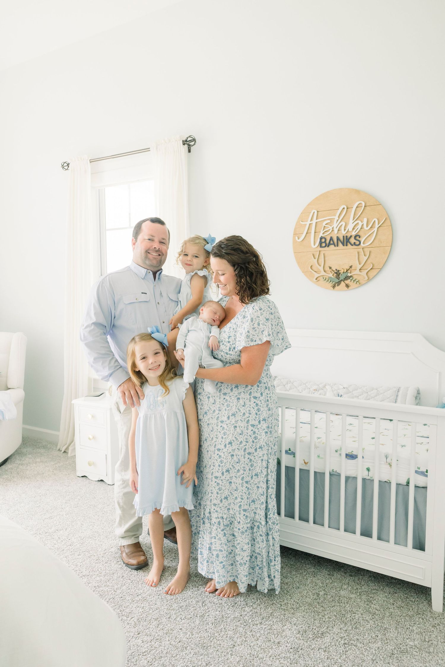 Family standing together in bright nursery with white crib and decorative wall art.