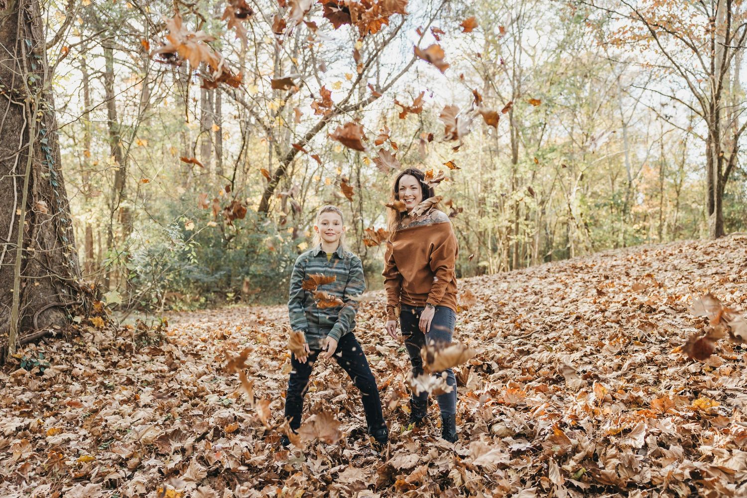 Two people playfully toss fallen leaves in the air during an autumn photoshoot.