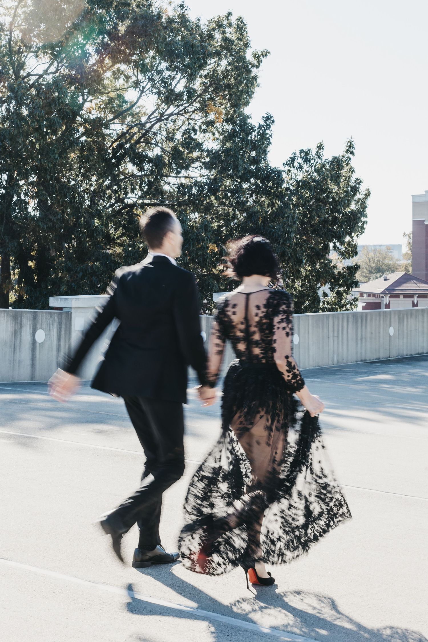 Dancing couple in formal wear twirls on outdoor terrace with trees in background.