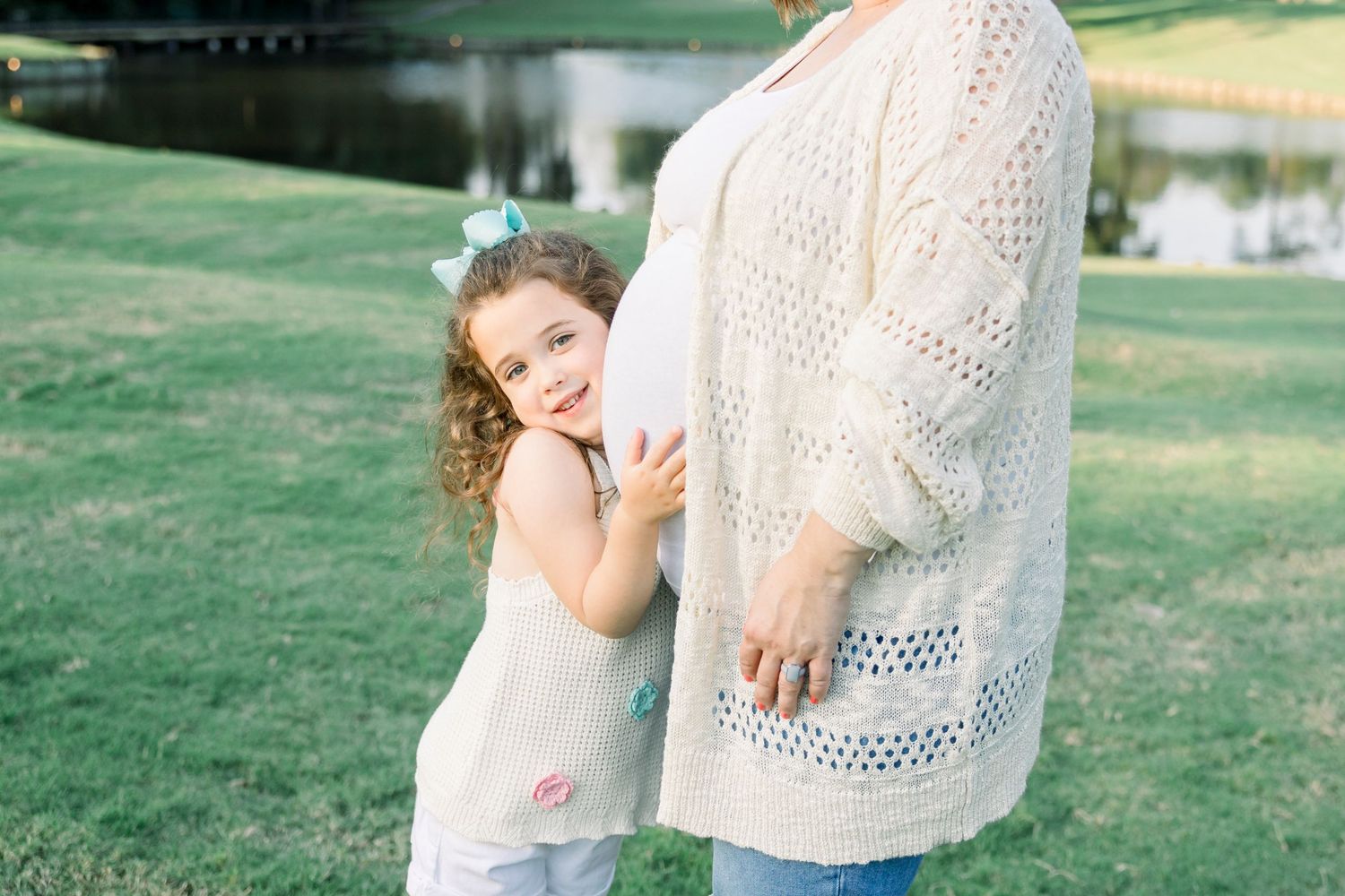 Family maternity photos in white lace dress on green lawn.