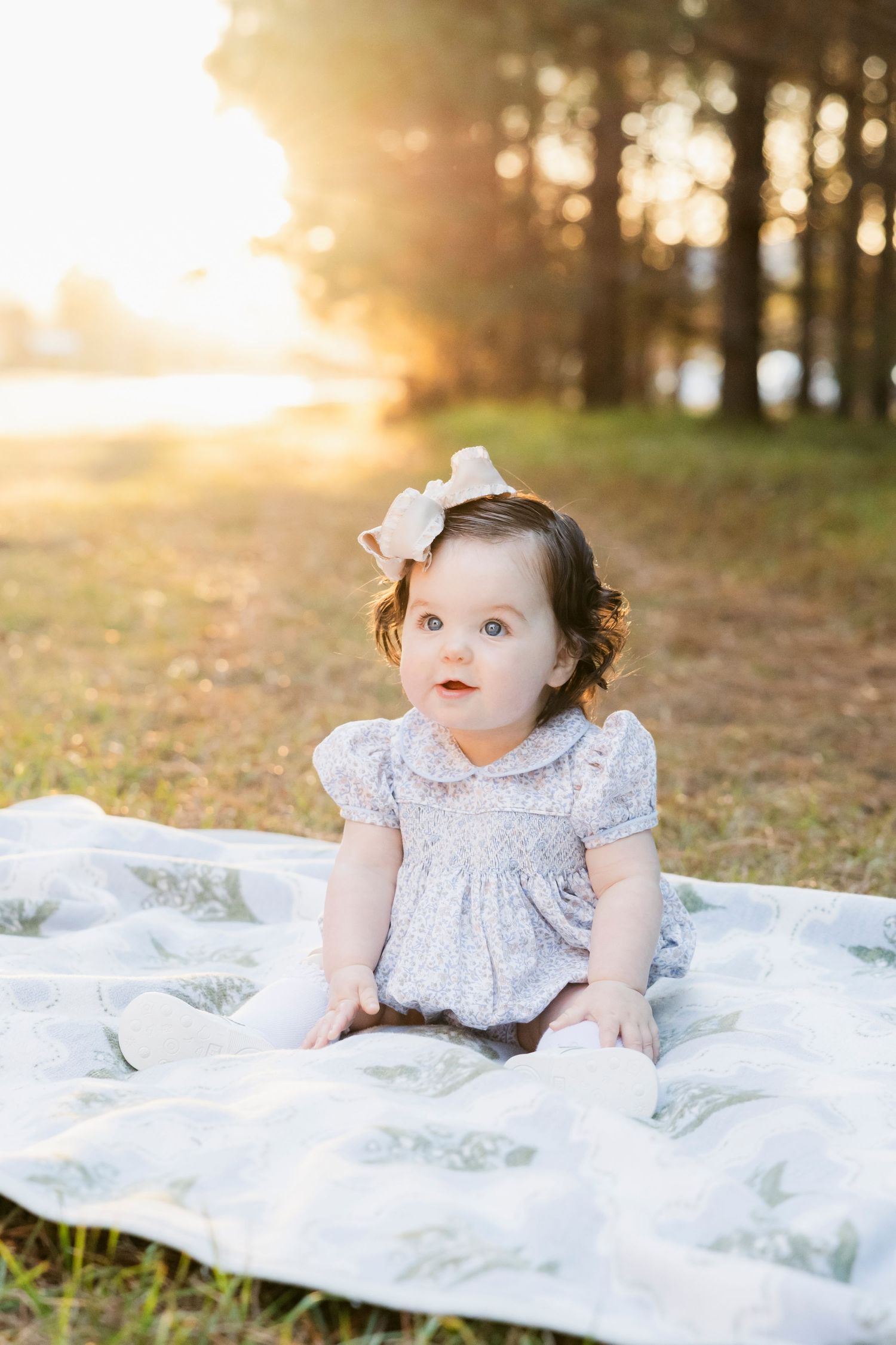 Baby in lace dress lies on white blanket during outdoor autumn photo session.