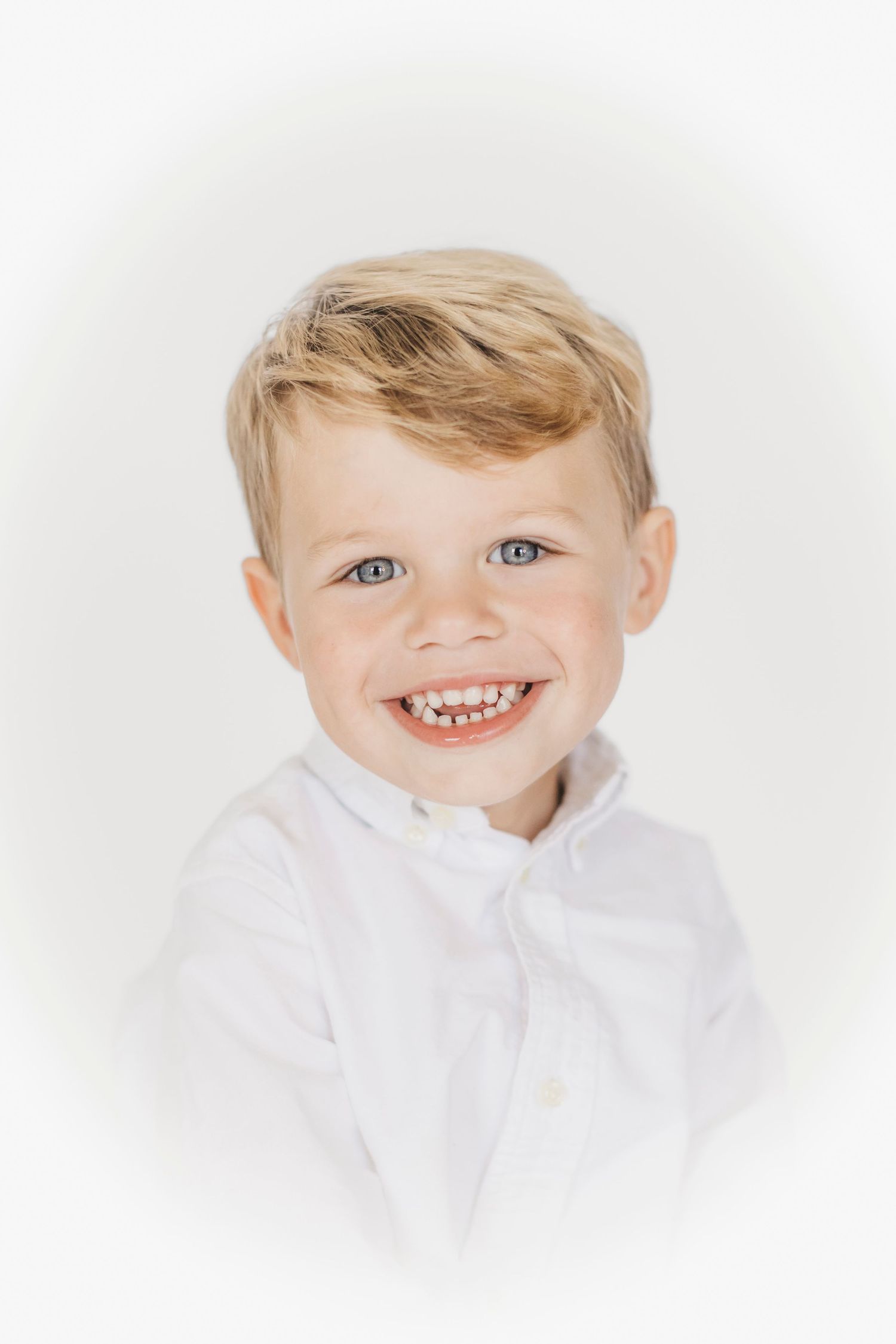 Close-up portrait of child in white collared shirt against bright white background.