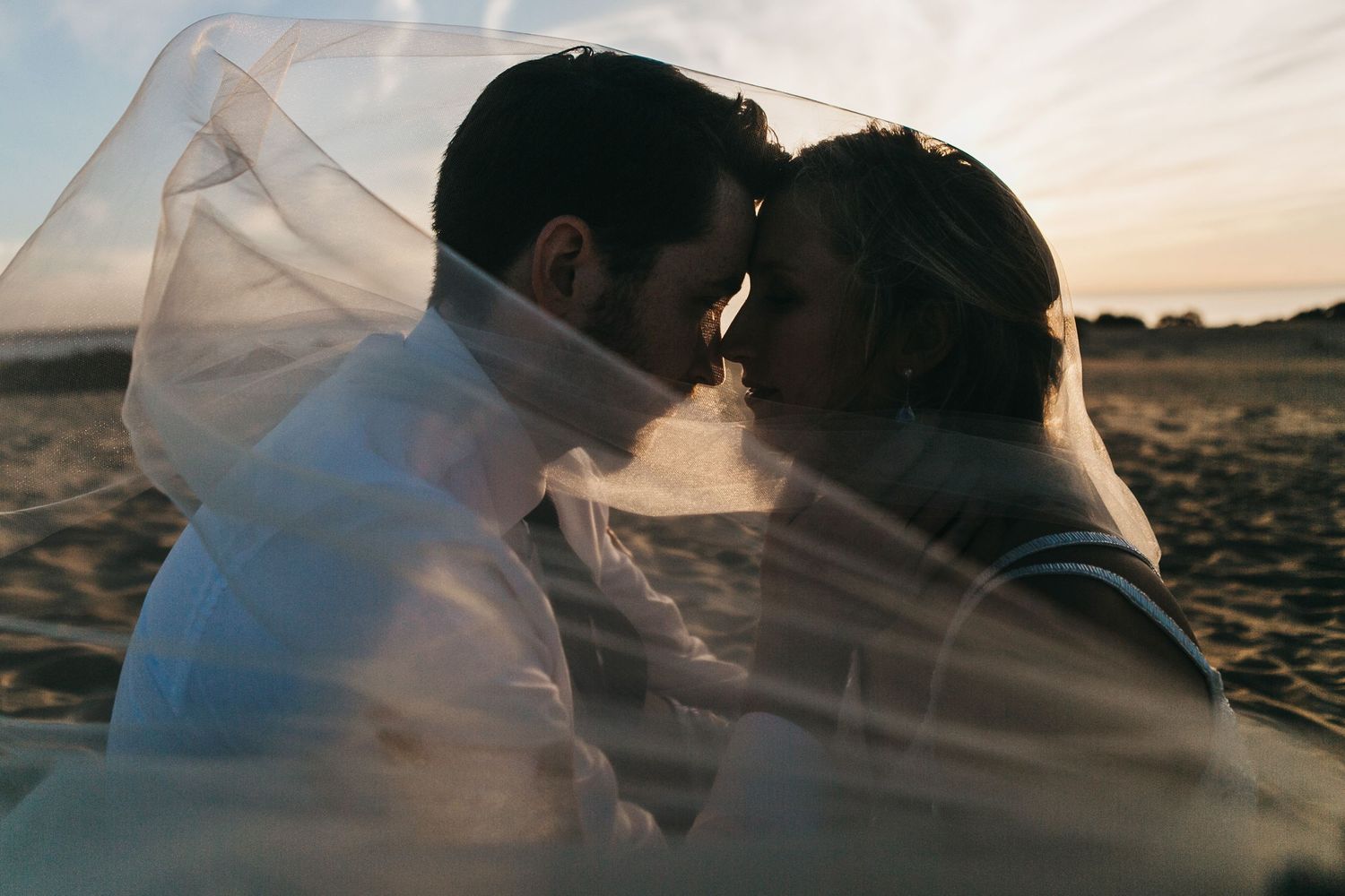 Romantic sunset beach photography with flowing veil creating artistic silhouettes.