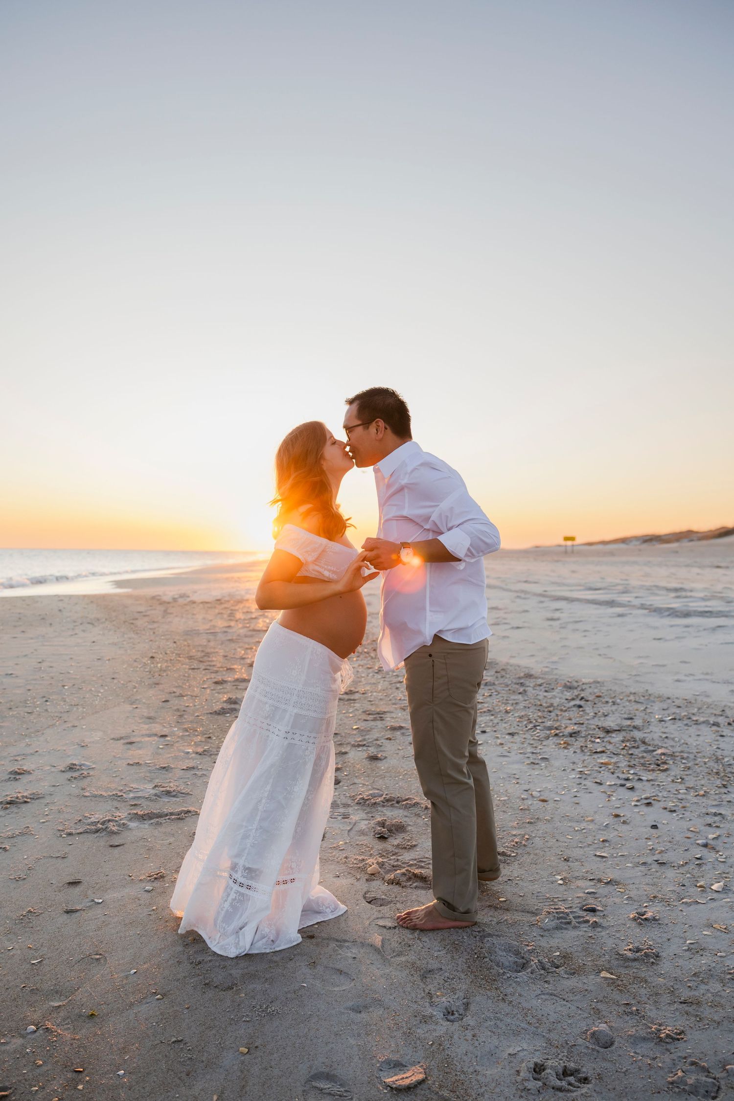 A couple embraces on a beach at sunset with golden light illuminating their silhouettes.