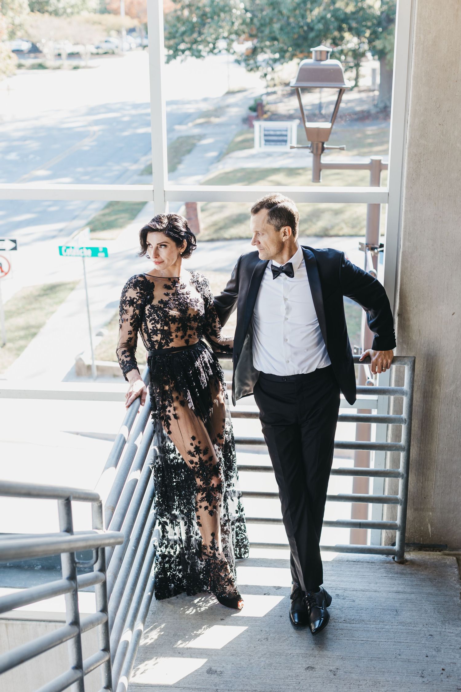 Couple dances playfully along covered walkway in formal attire.