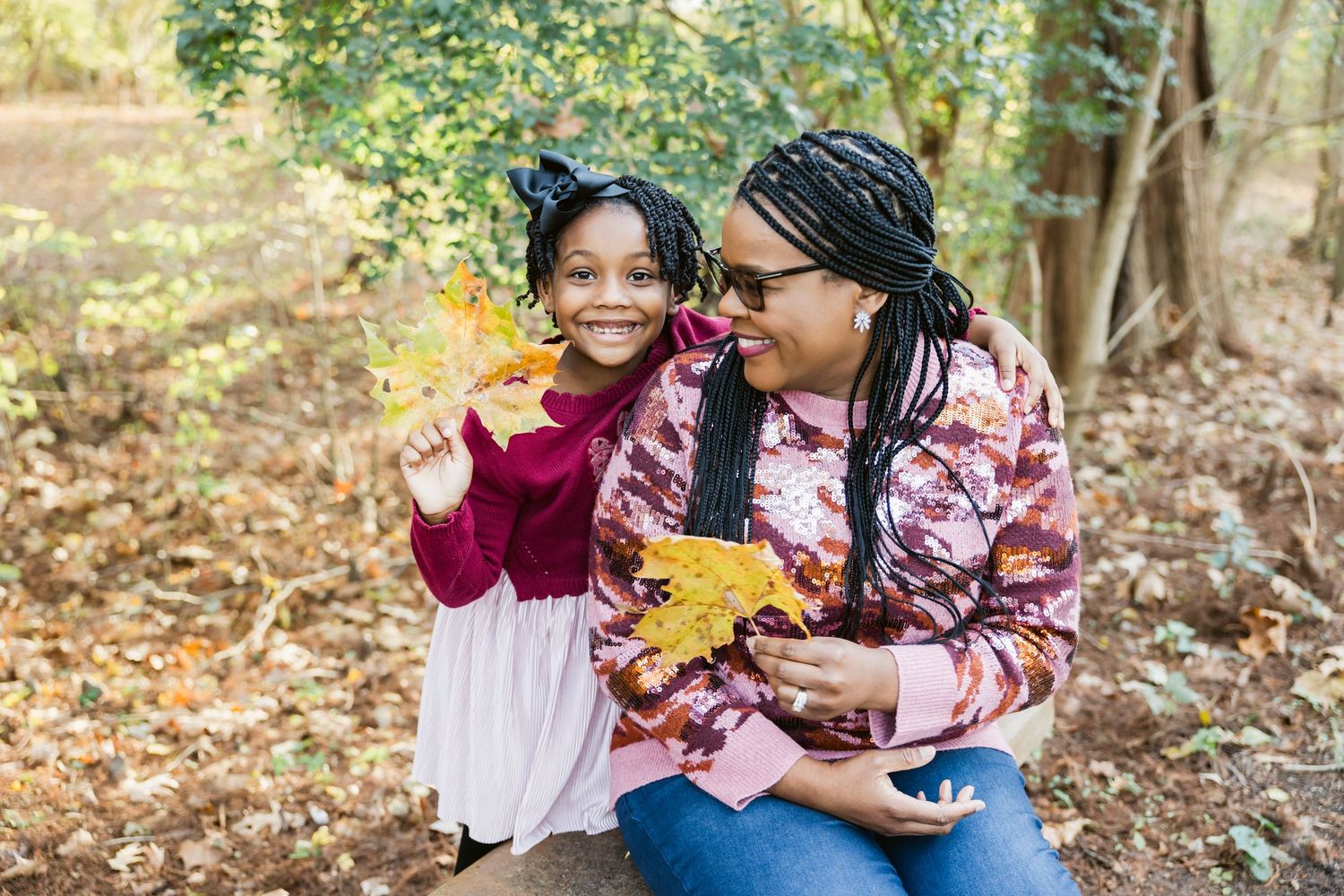 Two people share a joyful moment examining autumn leaves in a wooded setting.