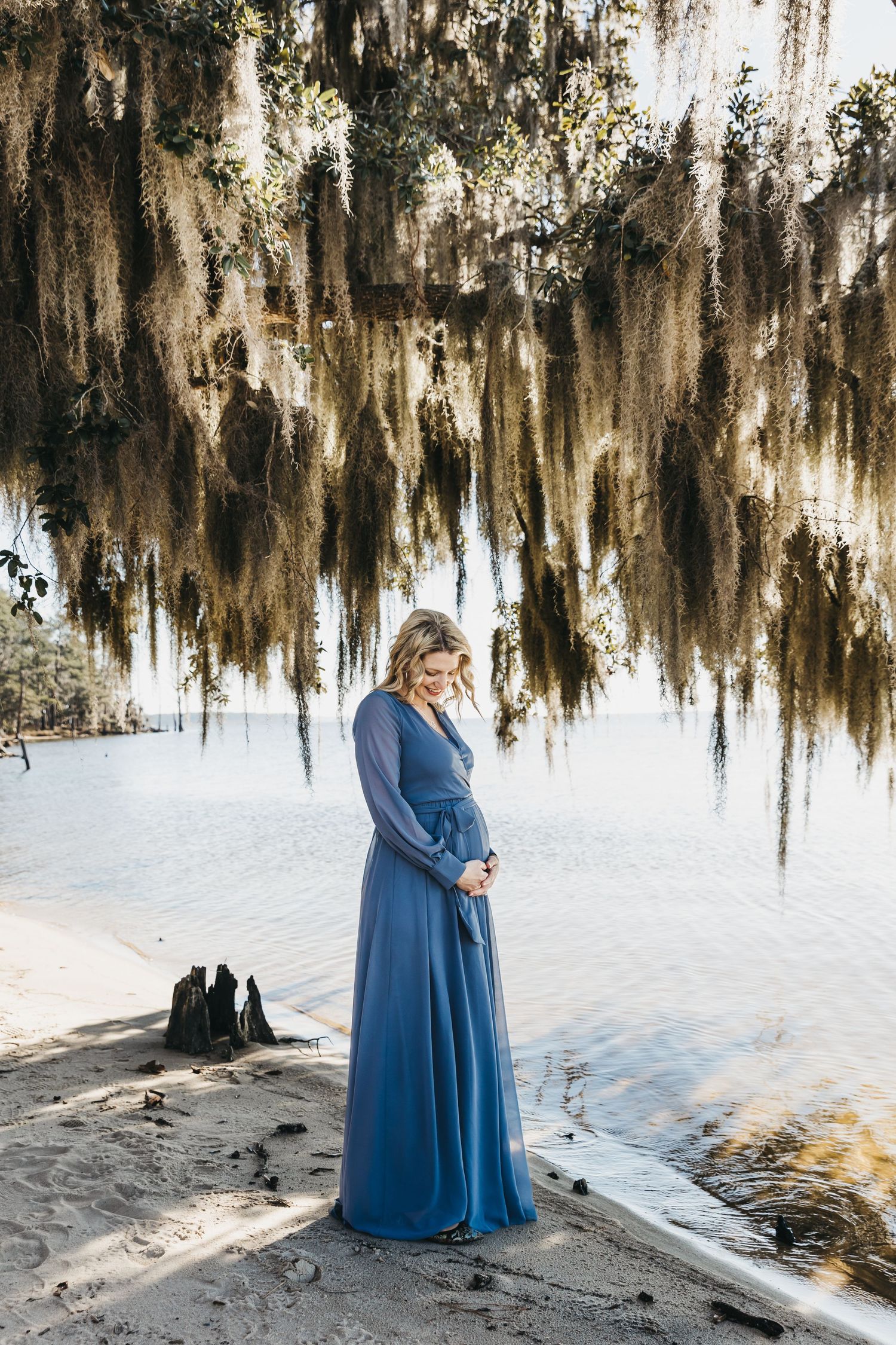Couple in matching blue outfits embrace under Spanish moss draped trees in romantic outdoor setting.