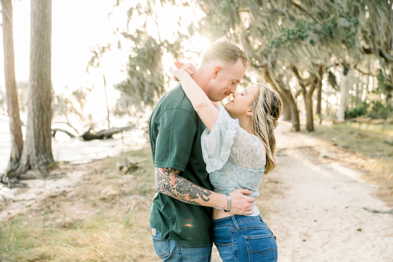 Couple sharing intimate moments on a tree-lined path during a sunny afternoon.